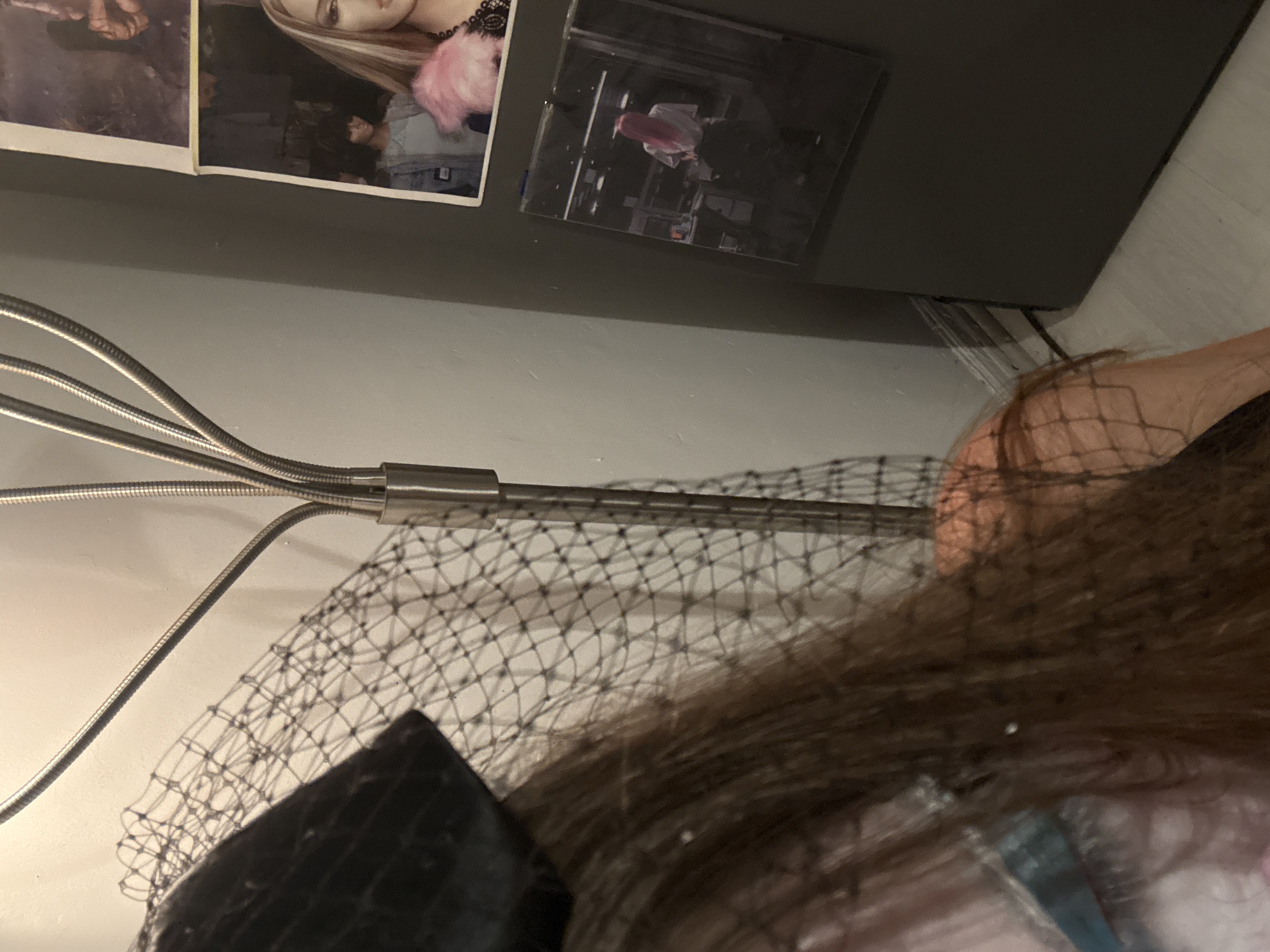 The image shows a partial view of a person wearing a black fascinator with netting over their brown hair. A chrome-colored lamp with multiple flexible arms is positioned near the person. The background includes a light gray wall with photographs or images attached. The location in Mexico City is not apparent from the image.