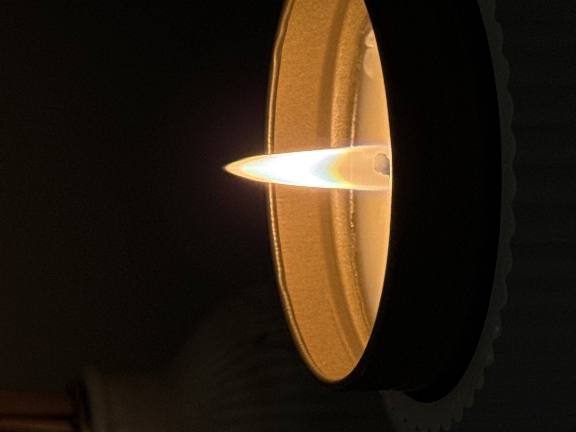 A gas fireplace insert is burning with a blue flame contained within a black circular frame with a gold interior. The background is dark. The location and city are unknown.