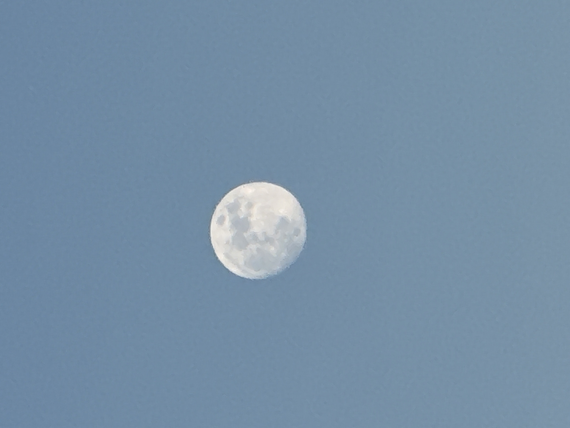 The image shows a full moon against a pale blue sky. No location information is present in the image.