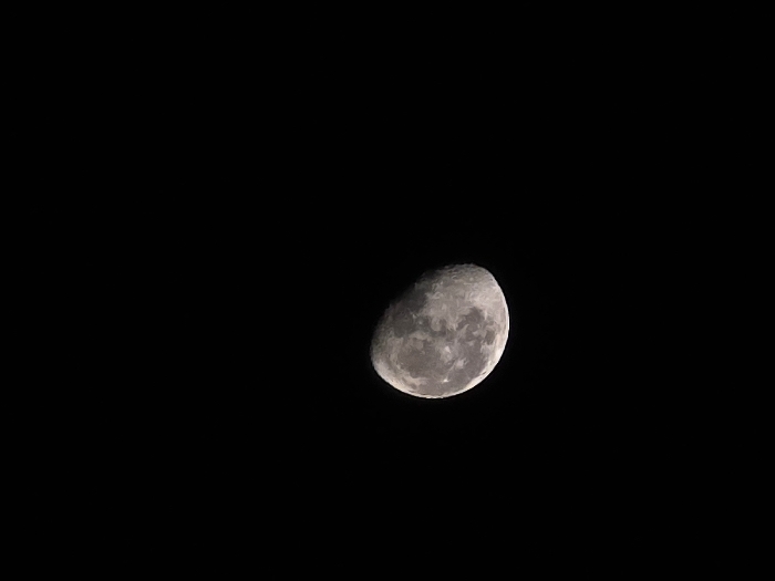 The image presents a celestial object, identified as the Moon, against a uniformly black background. The Moon is in a gibbous phase, approximately three-quarters illuminated, with the brighter portion visible on the right side. Surface features, including craters and maria, are discernible across the illuminated terrain. A distinct terminator line separates the lit and unlit portions of the lunar surface. The surrounding environment is completely dark, indicating a night sky devoid of other celestial bodies or atmospheric light pollution. No individuals, man-made objects, or actions are depicted within the frame. The observation point for this scene is the city of Yambol, Bulgaria.