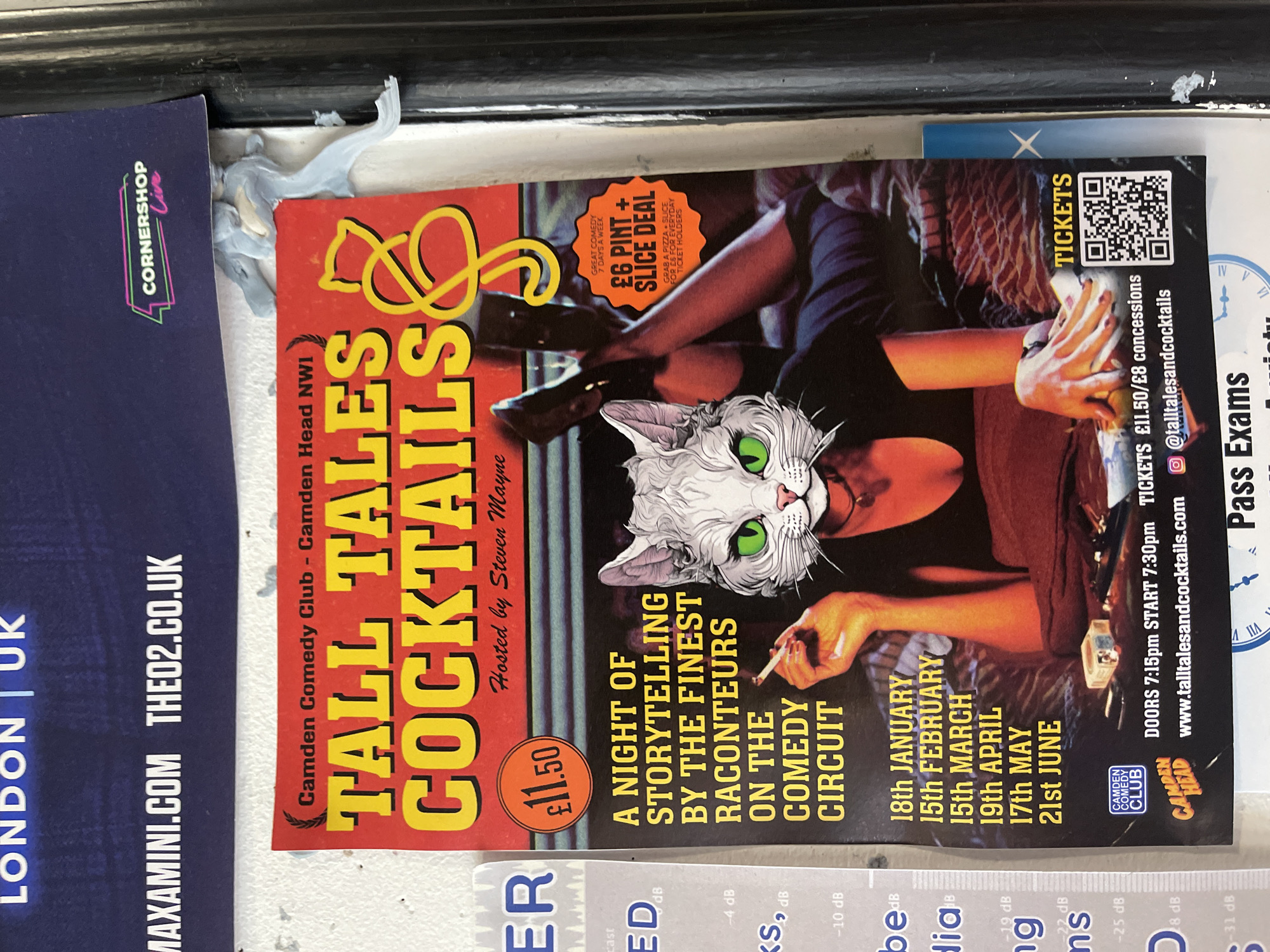 This image captures multiple overlapping posters, primarily featuring a vertically oriented advertisement for an event titled "Tall Tales & Cocktails." The main poster, photographed sideways, displays a distinctive imagery of a human body, possibly female, in a reclined pose, but with a cartoonish white cat's head featuring prominent green eyes. The figure appears to be holding a small object, possibly a cigarette, in one hand.
The event, "A NIGHT OF STORYTELLING BY THE FINEST RACONTEURS ON THE COMEDY CIRCUIT," is hosted by Steven Mayne and takes place at the Camden Comedy Club - Camden Head NW1, indicating a London, UK setting. Specific dates listed for the event include 18th January, 15th February, 15th March, 19th April, 17th May, and 21st June. Doors open at 7:15pm, with the show starting at 7:30pm. Tickets are priced at £11.50, with concessions available for £8. A promotional offer of "£6 PINT + SLICE DEAL" (pizza slice) is advertised for ticket holders, valid everyday as "GREAT COMEDY 7 DAYS A WEEK." A QR code for tickets and the website "www.talltalesandcocktails.com" and Instagram handle "@talltalesandcocktails" are visible.
Partially visible alongside the main poster are other advertisements. To the left, a blue poster mentions "CORNERSHOP Live," "LONDON | UK," and websites "MAXAMINI.COM THEO2.CO.UK." Below the main poster, fragments of text like "Pass Exams" and various decibel readings ("-4 dB," "-10 dB," "-19 dB," etc.) are discernible on another poster. The overall scene suggests a public display area for event promotions, likely indoors or a covered outdoor space, given the relatively clean condition of the posters.