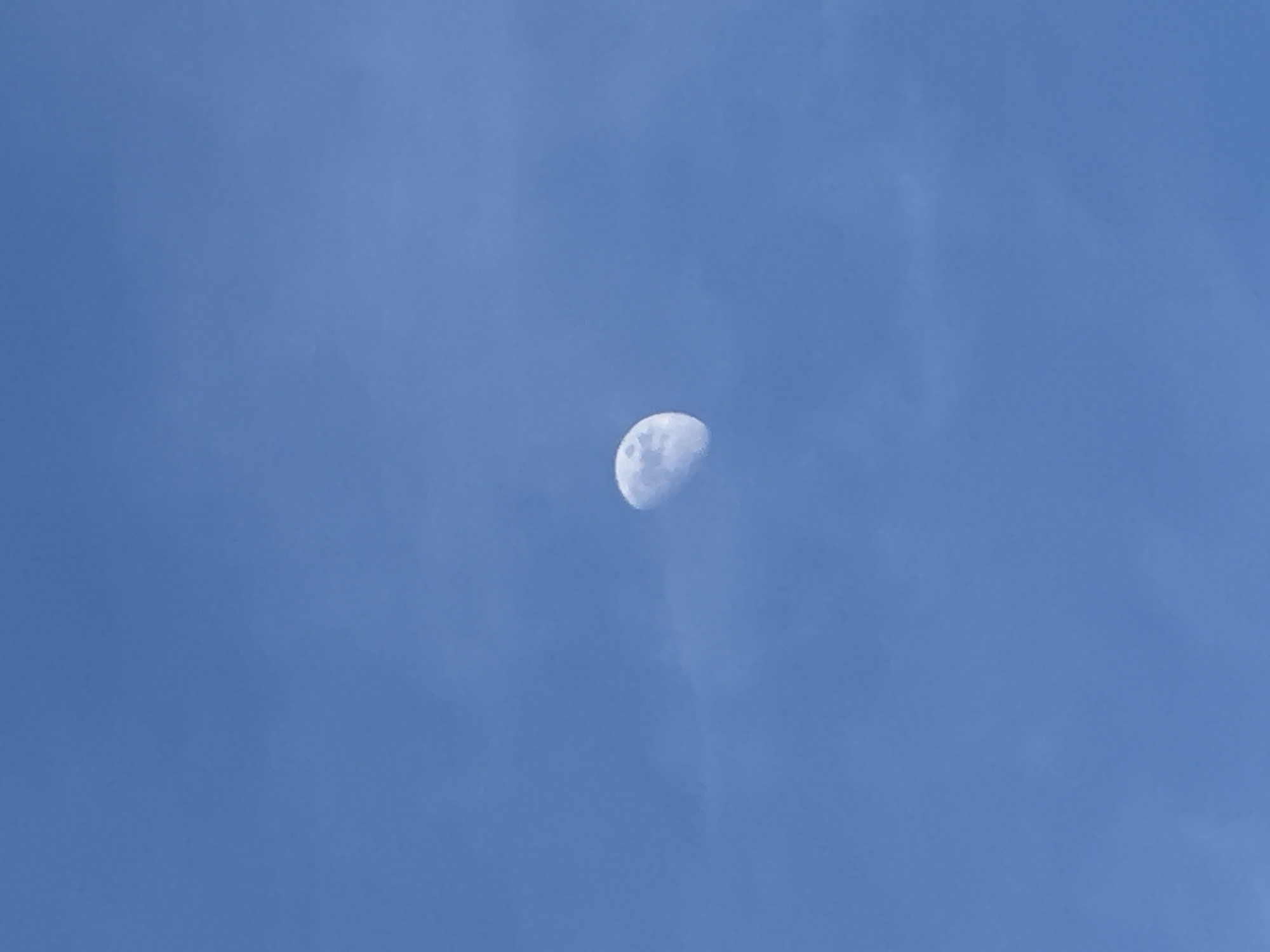 The image shows a crescent moon in a clear blue sky. No people, subjects, objects, actions, interactions or location information of the city of Sarnevo, Bulgaria can be seen in this image. The environment is characterized by a daytime sky with faint cloud texture.