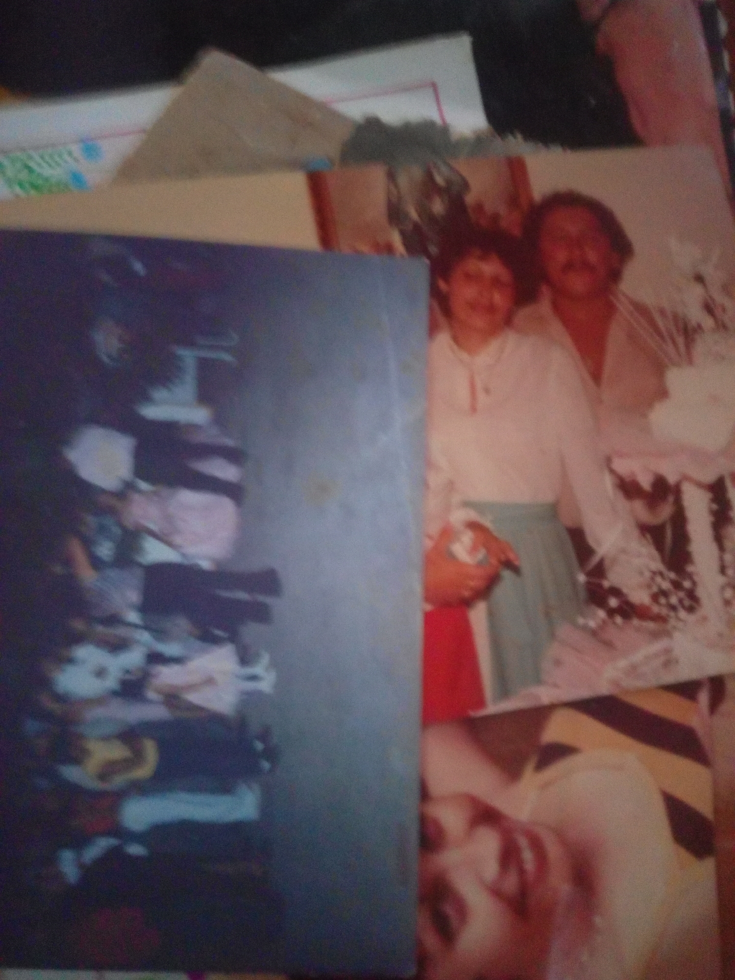 The image shows two photographs superimposed on each other. The top photograph depicts a woman and a man in what appears to be a formal setting. The woman is wearing a white top and a light blue skirt, holding a bouquet of flowers. The man is wearing a light-colored shirt. The background includes decorative elements suggesting a celebration or event.
The bottom photograph, on the left side of the image, shows a pile of clothing and other items, possibly in a storage or closet area. The items are varied in color and texture, and are stacked or folded.
There is no visible information within the image to determine the specific location in the city of La Tagua, Venezuela.
