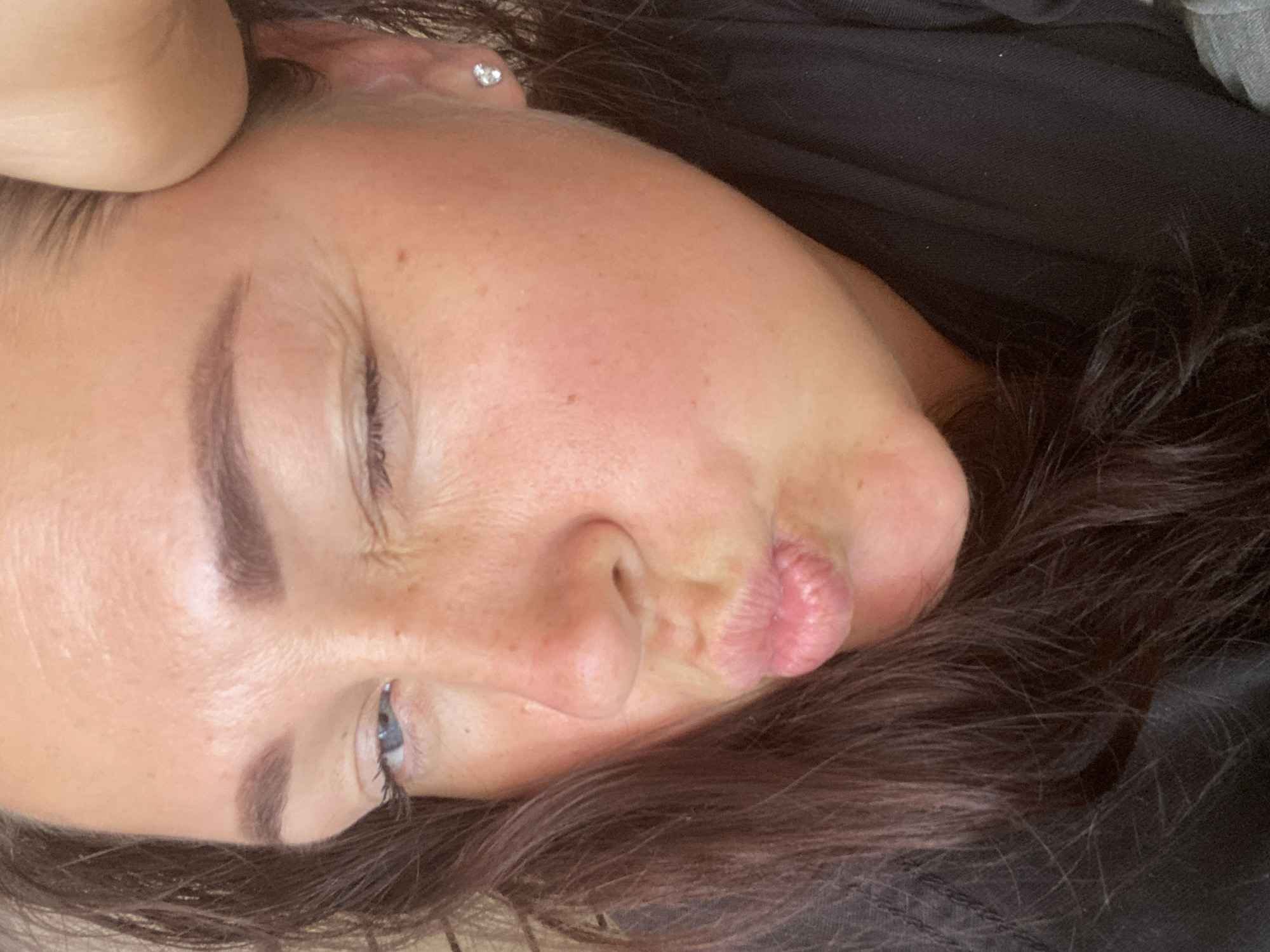 The image shows a close-up of a woman's face, with her right eye closed in a wink and her lips puckered. She has brown hair and fair skin with some freckles. She is wearing a black t-shirt and a diamond stud earring. Her hand is resting on her forehead. The image does not contain any information about the city of Sochi, Russia.