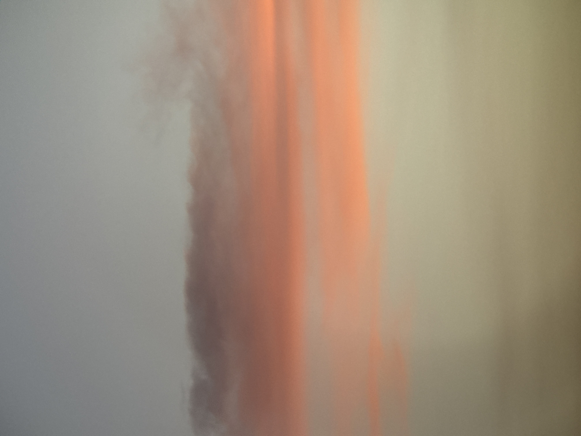 The image shows a sky with bands of clouds. The top portion of the sky is a muted gray, transitioning into streaks of pink and orange from the sunset. The lower portion of the sky is a light, hazy beige. The clouds appear wispy and diffuse, suggesting a warm, humid climate. While the image itself does not contain any specific landmarks or details to pinpoint its exact location within Nha Trang, Vietnam, the atmospheric conditions are consistent with those found in coastal tropical regions during twilight hours. There are no people, subjects, or objects visible in the frame.