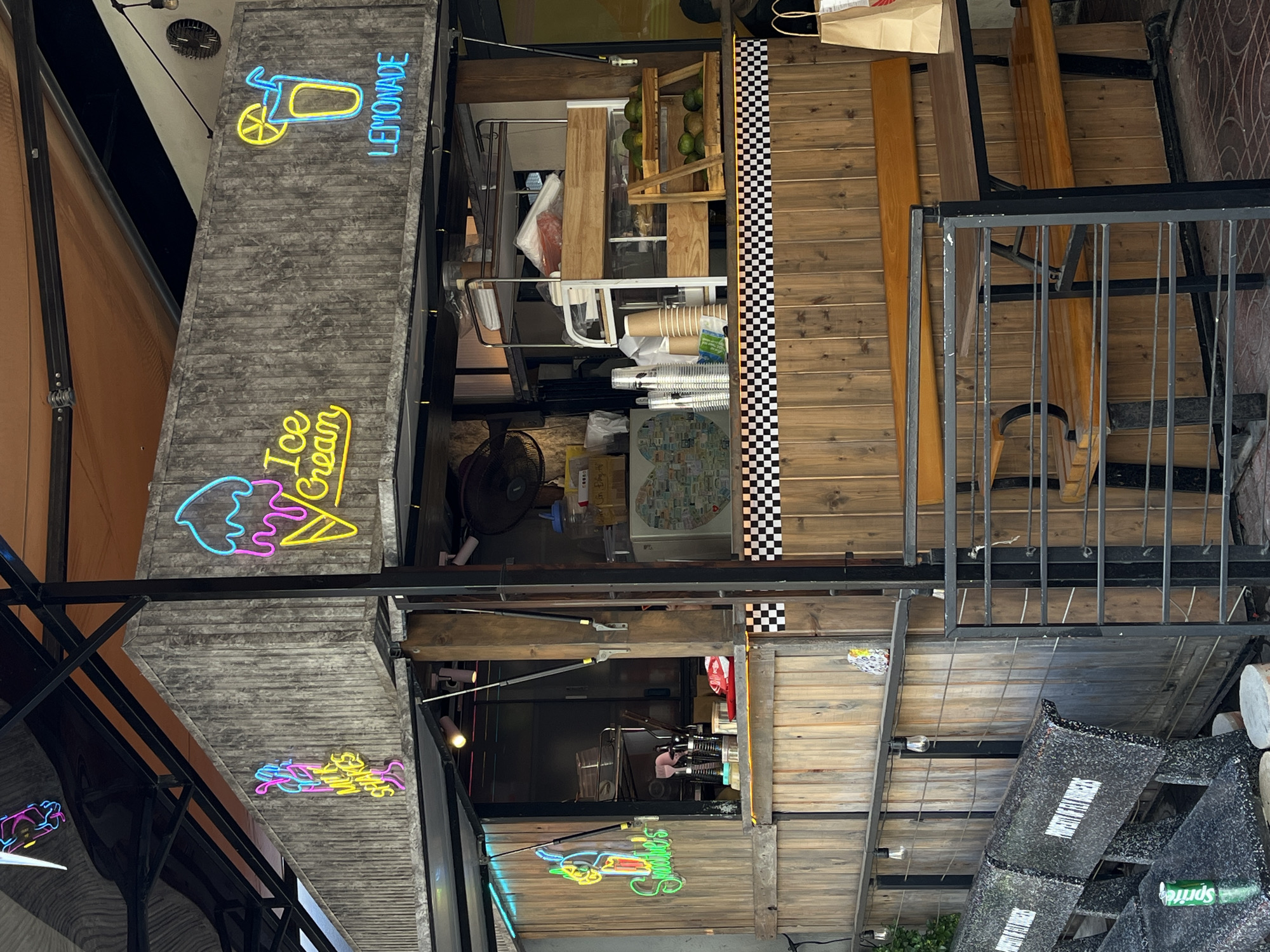 The image depicts a multi-story building facade in Đà Nẵng, Vietnam. A small business occupies the structure, indicated by neon signs advertising "Lemonade" and "Ice Cream." The building features a mix of construction materials, including wood paneling, concrete, and metal. The upper floors contain storage and service areas. The overall environment suggests a commercial district.