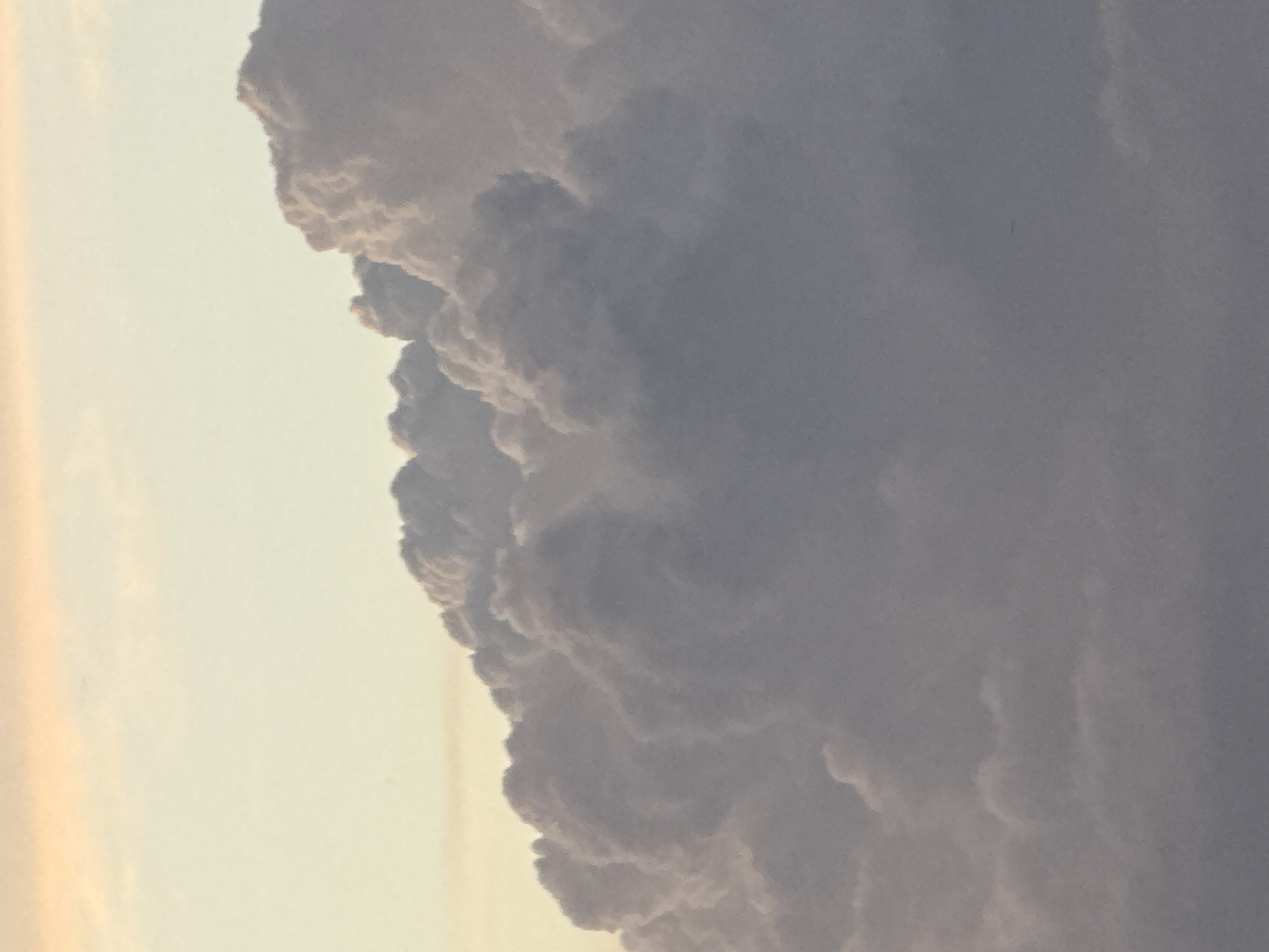 A close-up, low-angle, vertical shot captures a dramatic formation of cumulonimbus clouds against a pale, soft-yellow sky. The clouds are dense and voluminous, with shadowed undersides and brightly illuminated, textured tops, suggesting a late afternoon or early morning light source. The overall tone is muted, with subtle variations in gray and off-white, creating a sense of depth and scale. The image is devoid of any human presence, structures, or terrestrial landscape, focusing solely on the atmospheric phenomenon. The location of Stony Plain, Canada, is not visually represented in this image.