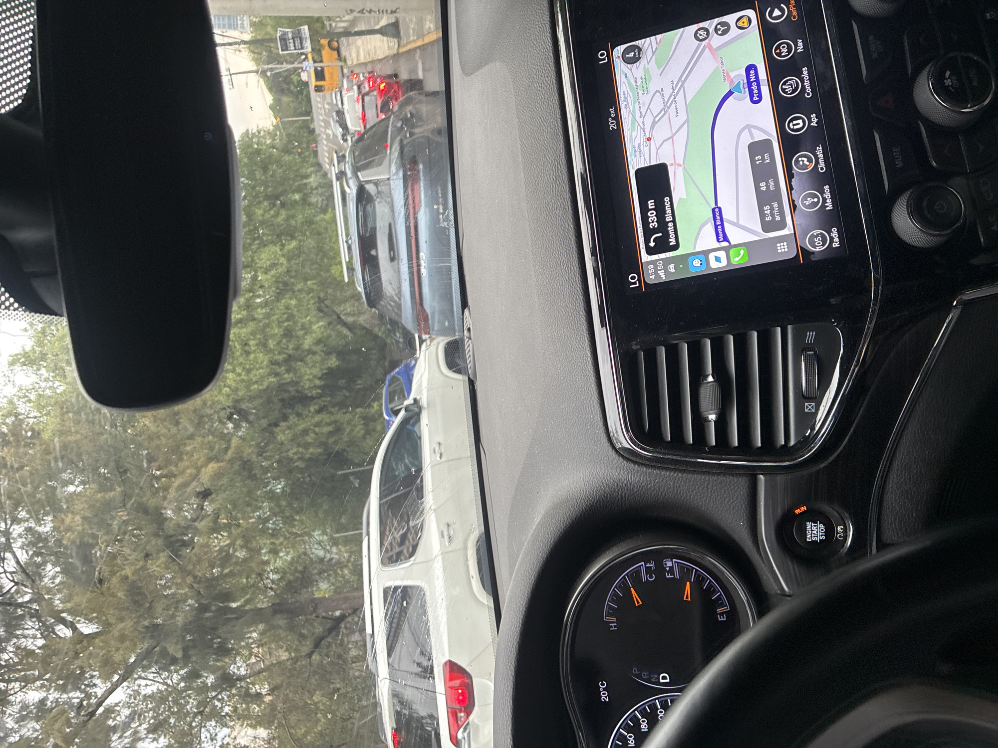 The image shows the interior of a vehicle, likely a car, with a view of traffic outside the windshield. The navigation system on the dashboard indicates the vehicle is approximately 330 meters from Monte Blanco, a location in Mexico City, Mexico. The time on the navigation system is 4:59, with an estimated arrival time of 5:45, suggesting a 46-minute commute over 13 kilometers. The fuel gauge shows the car has a full tank of gas. Traffic outside appears congested, consisting of multiple vehicles. The view through the windshield also includes trees lining the street.