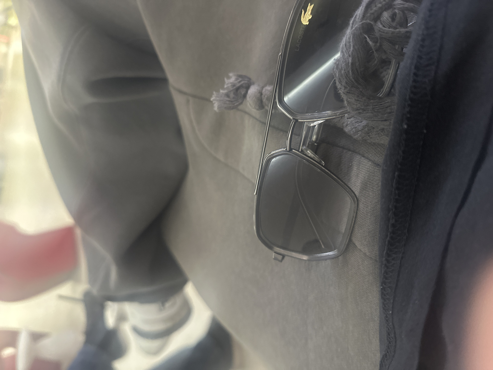 The image shows a close-up of a person wearing grey sweatpants and a dark-colored t-shirt. A pair of Lacoste sunglasses is hooked onto the sweatpants. In the background, a shoe with a blue and white color scheme is partially visible. The exact location in Yerevan, Armenia, is not identifiable from the image.