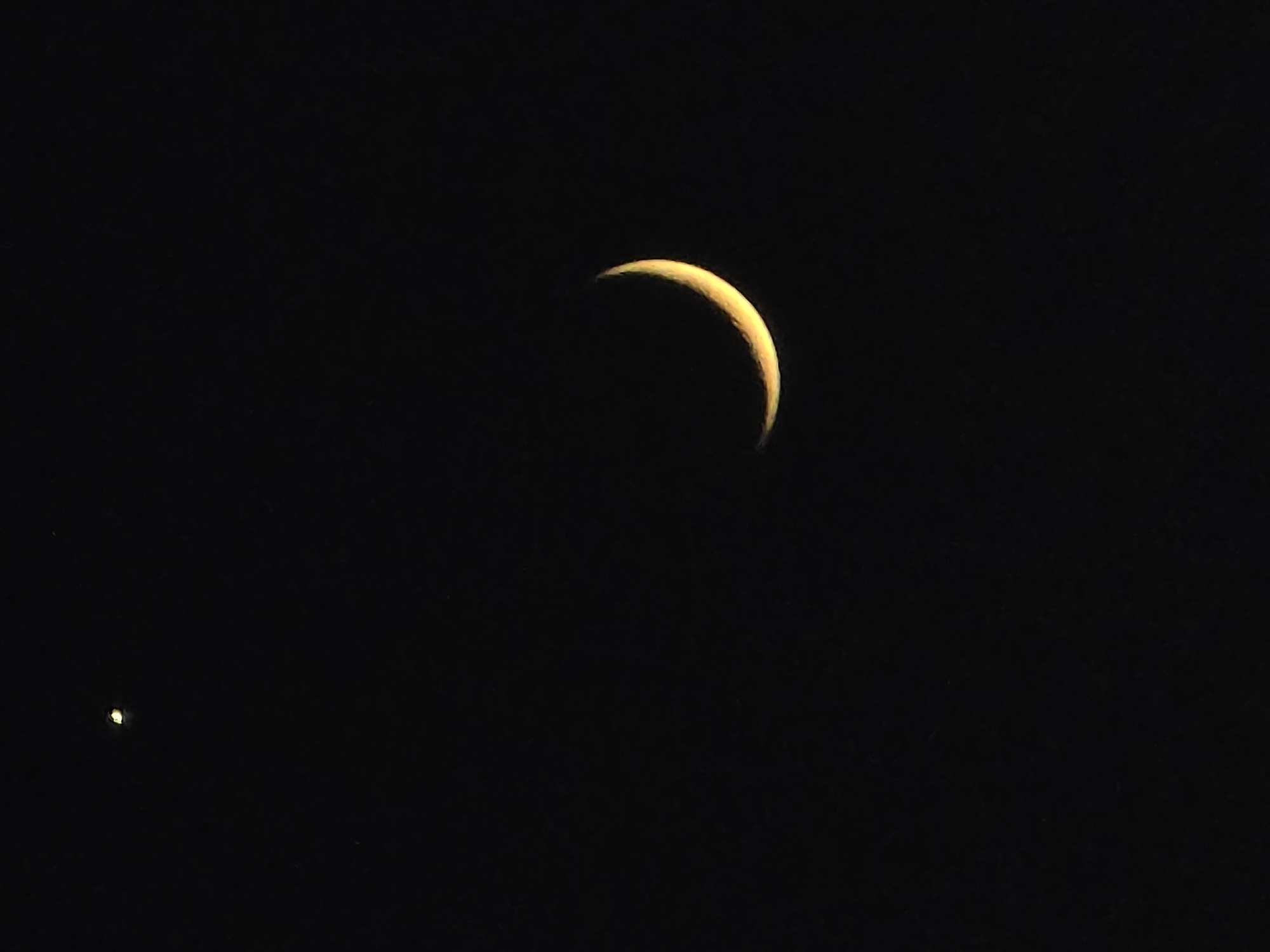 A sliver of a crescent moon is visible against a dark night sky. To the left of the moon, a bright point of light, likely a planet or star, is also present. The image was captured in Salerno, Italy.