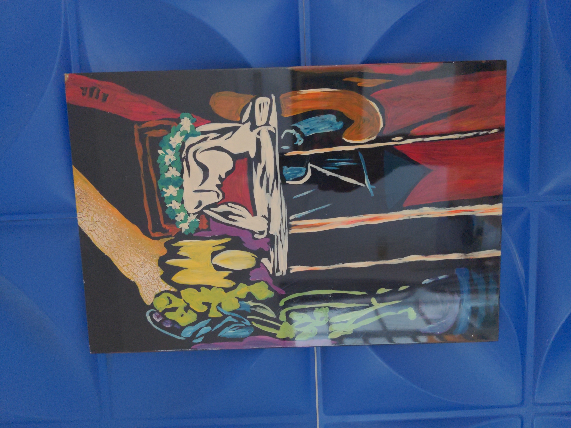 A rectangular framed painting hangs against a blue textured wall. The artwork depicts a boxing scene with bold, contrasting colors. A boxer, wearing a white robe and a garland of white flowers, is positioned on the left side of the painting. The right side of the painting shows the corner of a boxing ring with ropes and a red backdrop. The foreground features abstract shapes and colors, including yellows, greens, and purples, possibly representing the canvas or ground. The signature "JFJL" is visible in the upper left corner of the painting.
The location is Bac Nha Trang Ward, Vietnam.