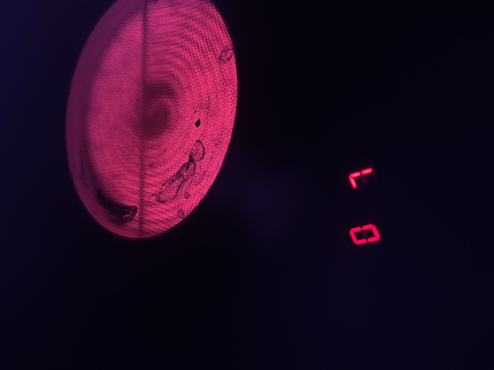 The image shows a close-up of a stovetop burner that is illuminated with a bright pink light. The burner has a textured surface with a circular pattern and appears to be slightly dirty. Below the burner, two red LED digits are visible: a "0" and a "7". The background is dark and out of focus. The scene is indoors, likely in a kitchen. There are no people or animals visible in the image. The location of Blagoevgrad, Bulgaria is not determinable from the image itself.
