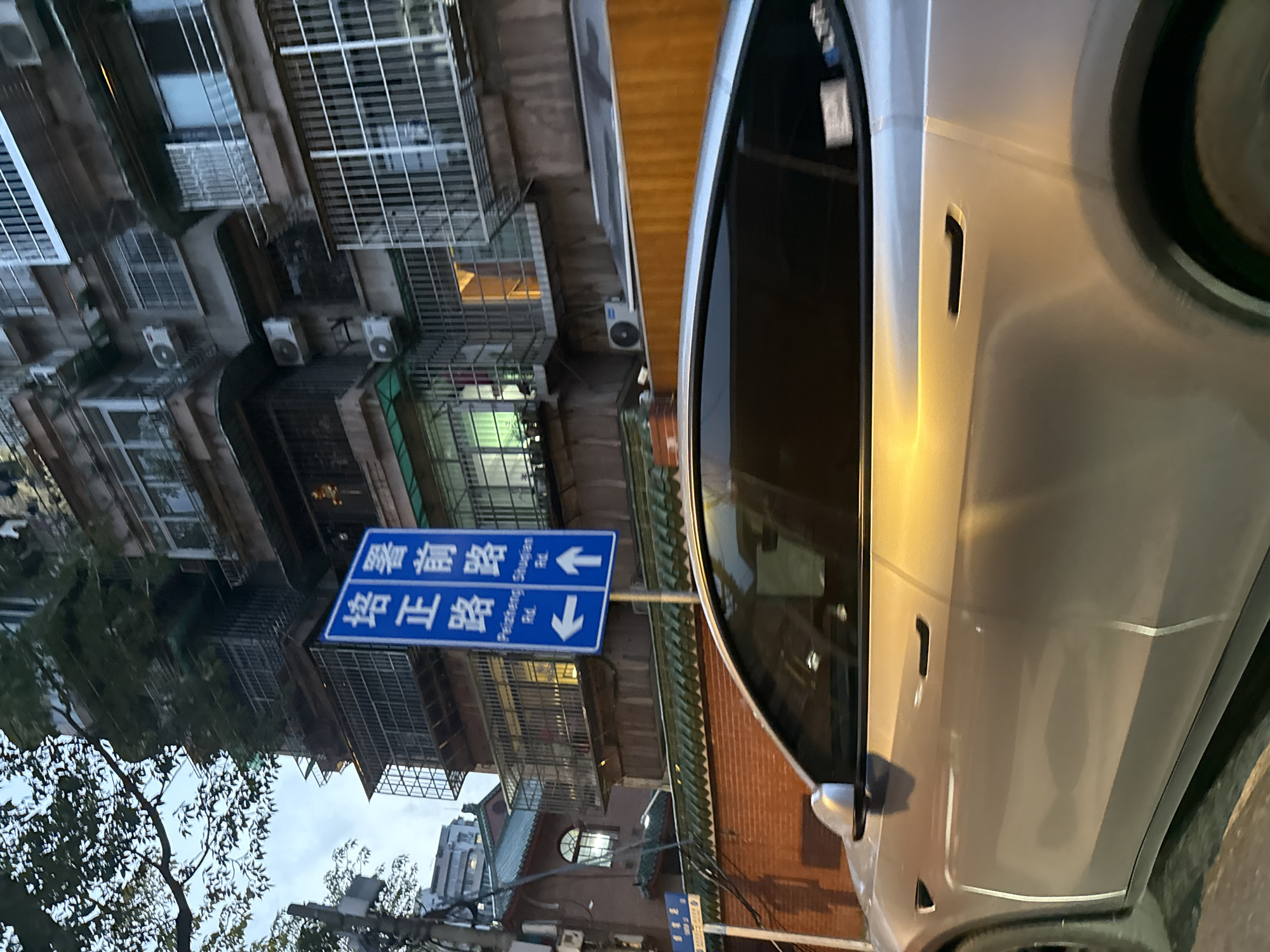 The image captures a street scene in Haizhu District, China. A silver car is parked on the right side of the frame. A blue street sign indicates the directions for "Ruijin New Road" and "Pengzheng Road." The background features older apartment buildings with metal window grilles and air conditioning units. The sky is overcast, suggesting a relatively quiet day.