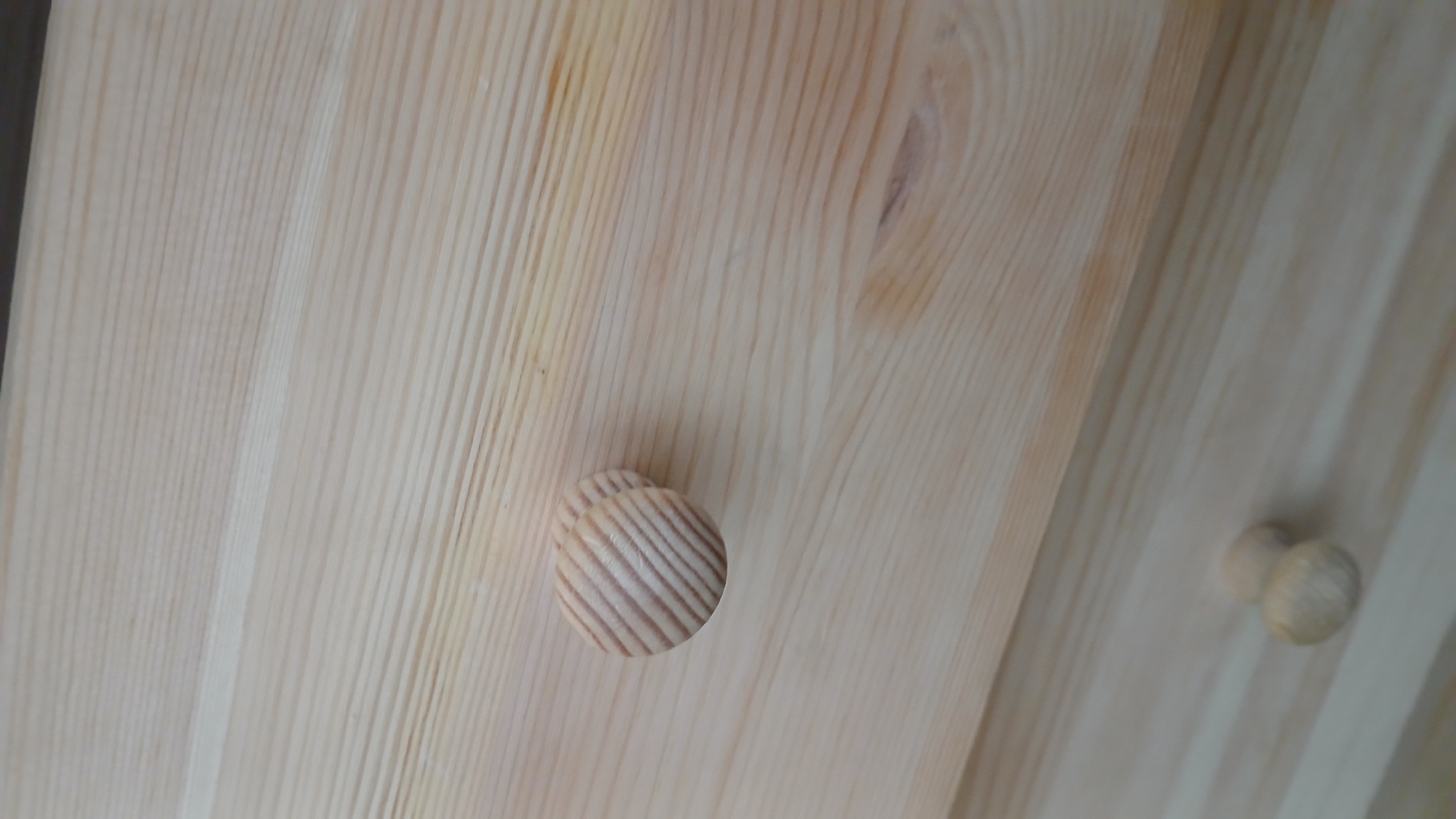 A close-up, angled shot showcases two wooden drawer knobs mounted on a light-colored wooden surface. The surface exhibits distinct wood grain patterns, characterized by parallel, thin lines of varying shades of tan and beige. The top knob, prominently positioned on the right side of the frame, is round and features a spiral pattern of alternating light and dark wood grain. The second knob, slightly out of focus and positioned below and to the left of the first, appears to be the same style but is less detailed due to its blurriness. The lighting suggests an indoor setting, casting subtle shadows and highlighting the texture of the wood. The image's context within Rubtsovsk, Russia, is not discernable from the visual information provided.