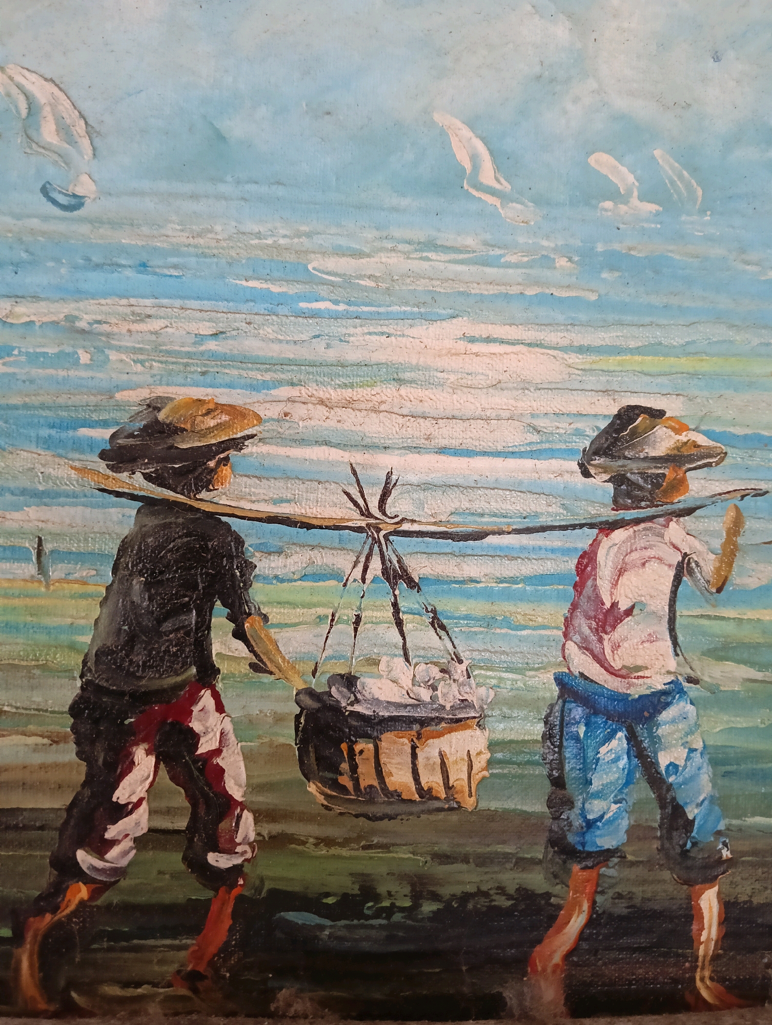 The painting depicts two individuals walking side-by-side, carrying a basket suspended from a pole balanced across their shoulders. The person on the left wears a dark shirt, red and white patterned pants, and a straw hat. The person on the right wears a light-colored shirt with red markings, blue pants, and a dark hat. Both are barefoot. The environment suggests an outdoor setting, possibly near water, with a textured blue and white sky above and a greenish-brown ground below. The style is impressionistic, with visible brushstrokes. The image is a painting, not a photograph.