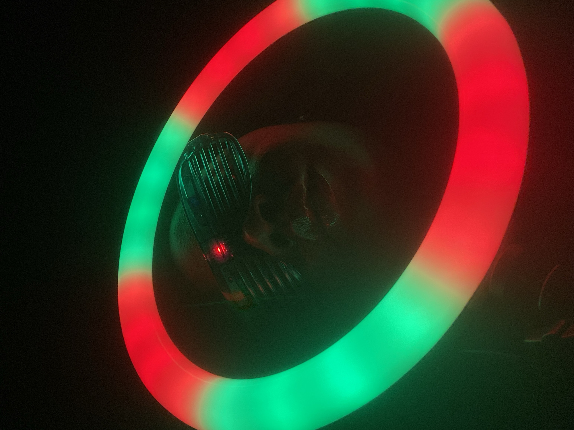 The image shows an illuminated red and green ring light surrounding what appears to be a human skull or a skull-like mask with a metallic grill over the face, viewed in a dark setting. The details of the skull or mask are difficult to discern due to the darkness and the lighting. The presence of the red and green ring light suggests an artificial or staged lighting situation. The image does not contain any information about the city of Maigizo, Nigeria.