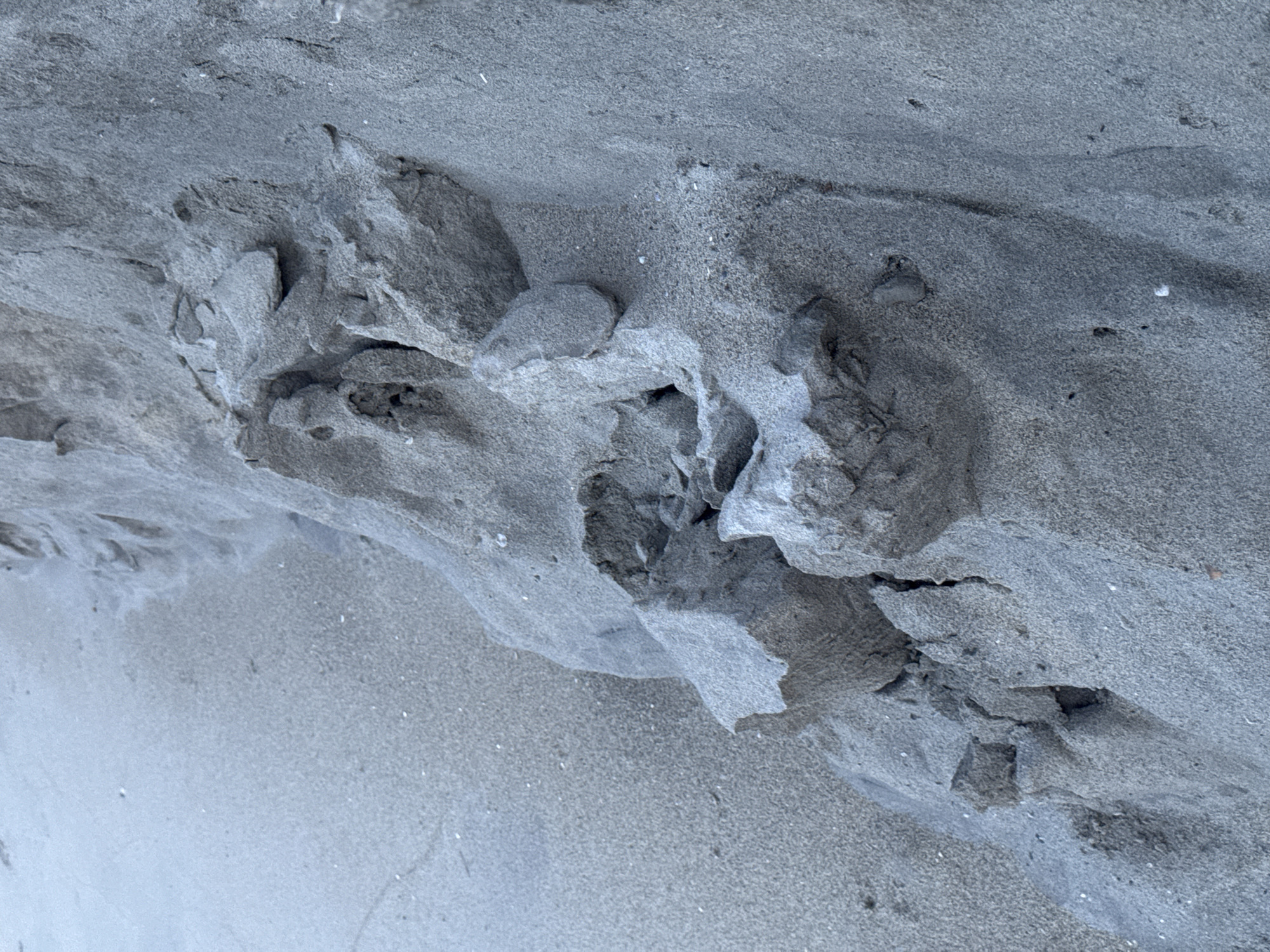 The image shows a close-up of a sand formation. The sand is a uniform gray color. The formation has various crevices and small rocks embedded in it. The photo is taken at an angle so that the sand stretches from the upper left to the lower right corner. The overall scene suggests a beach or coastal environment. It's impossible to verify the location is Đà Nẵng, Vietnam, with only this image.