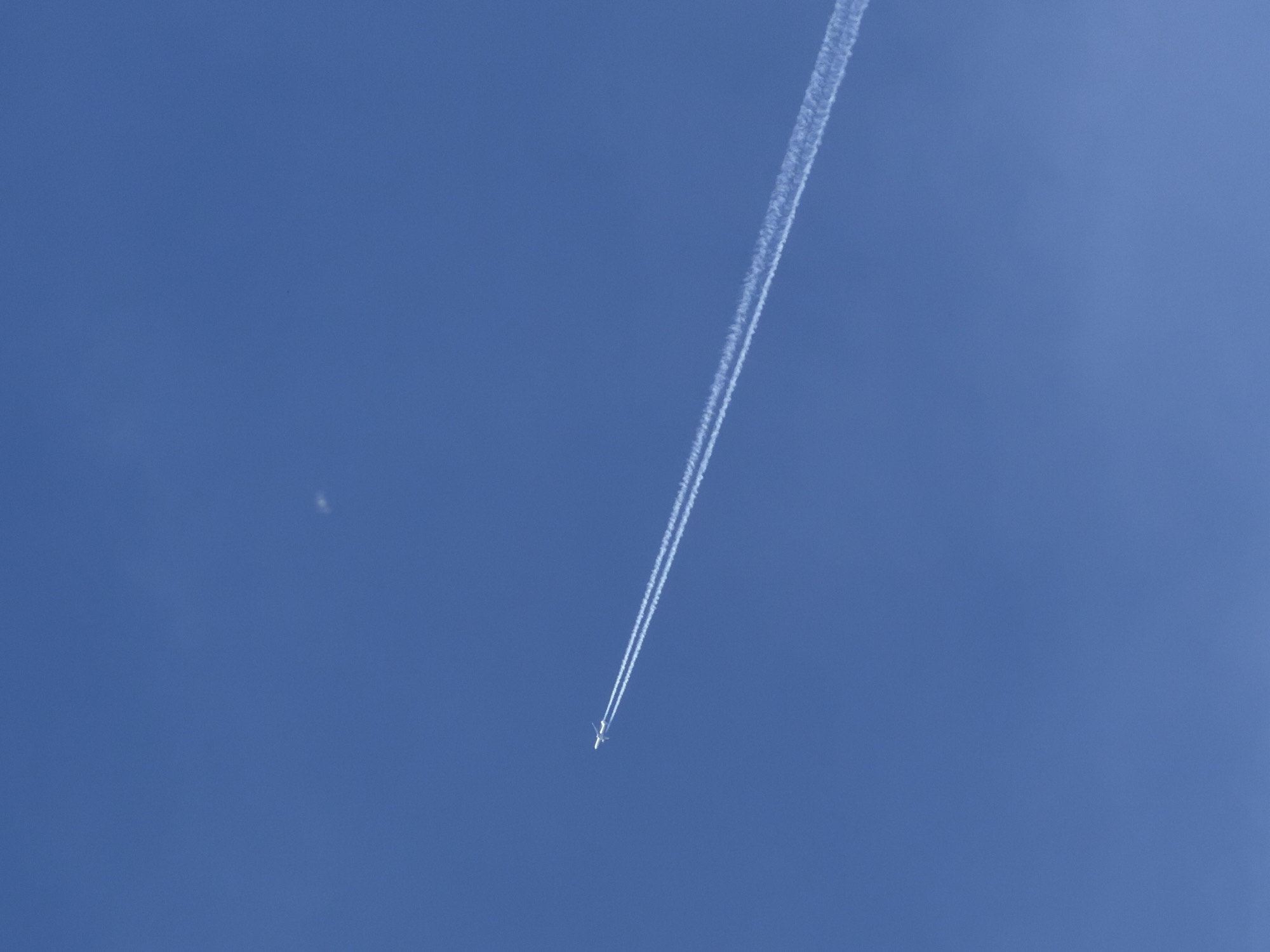 The image shows a commercial airplane flying in a clear blue sky, leaving a long contrail behind it. The location cannot be determined from the image alone. There is no evidence it is in Chaikovsky, Russia.