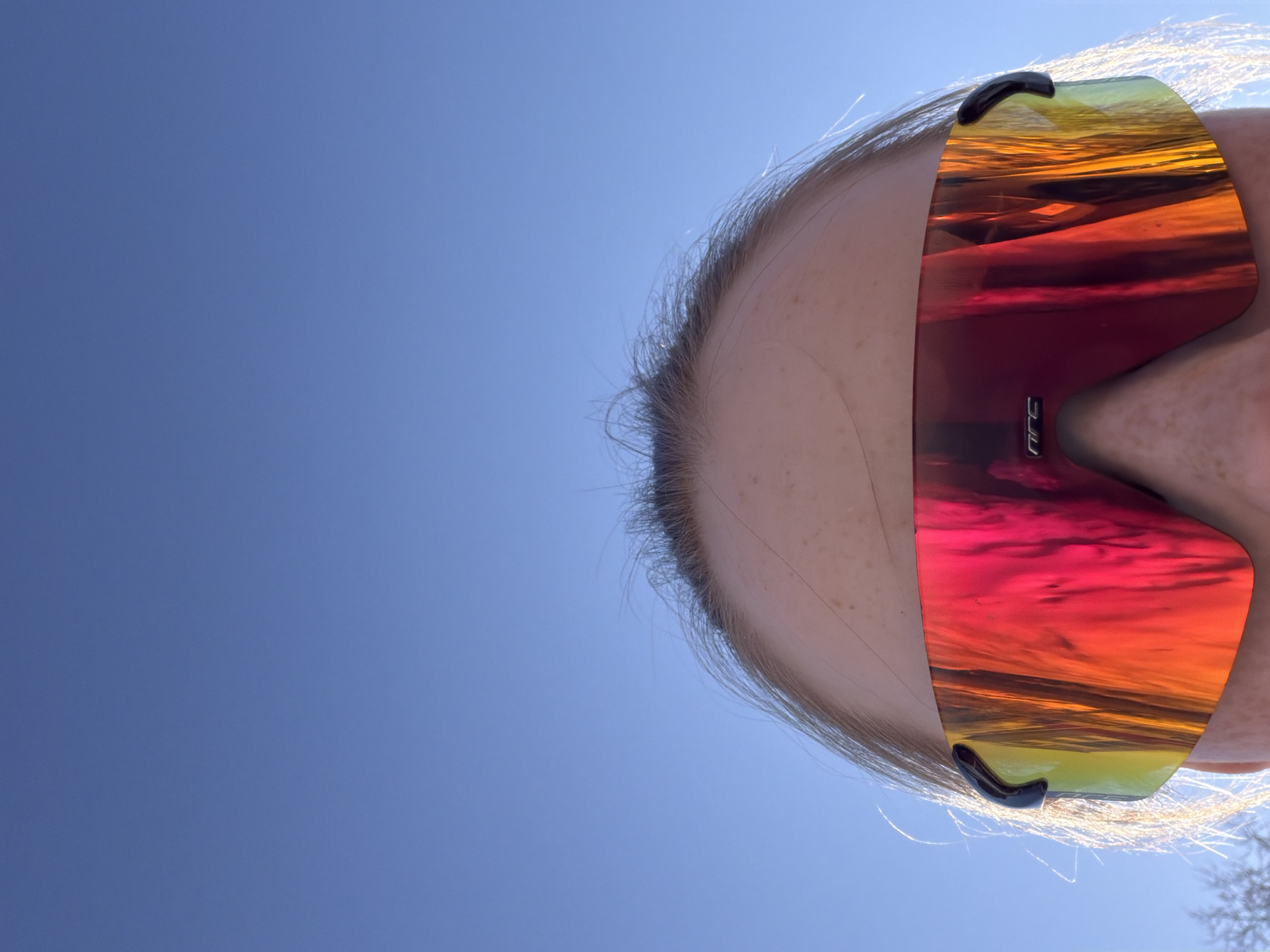 A low-angle shot looking up at a person wearing sunglasses. The lenses of the sunglasses have a gradient of colors ranging from yellow to orange to red. The sky is blue and cloudless. Berezniki, Russia cannot be determined from the given image.