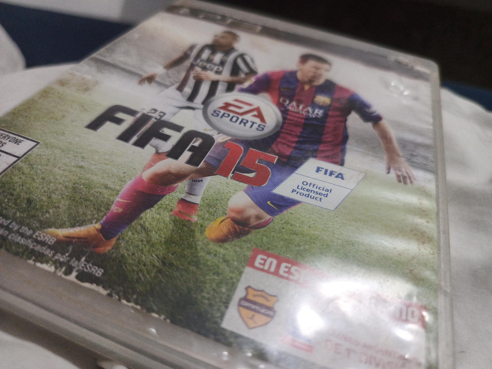The image shows a FIFA 15 video game cover. Lionel Messi in a Barcelona kit is featured prominently alongside another player in a Juventus jersey. The cover also displays the EA Sports logo and FIFA branding. The presence of "EN ESPAÑOL" suggests a Spanish language version. The scene is a close-up shot of the video game cover. The location in Los Robles, Venezuela is not discernible from the image.
