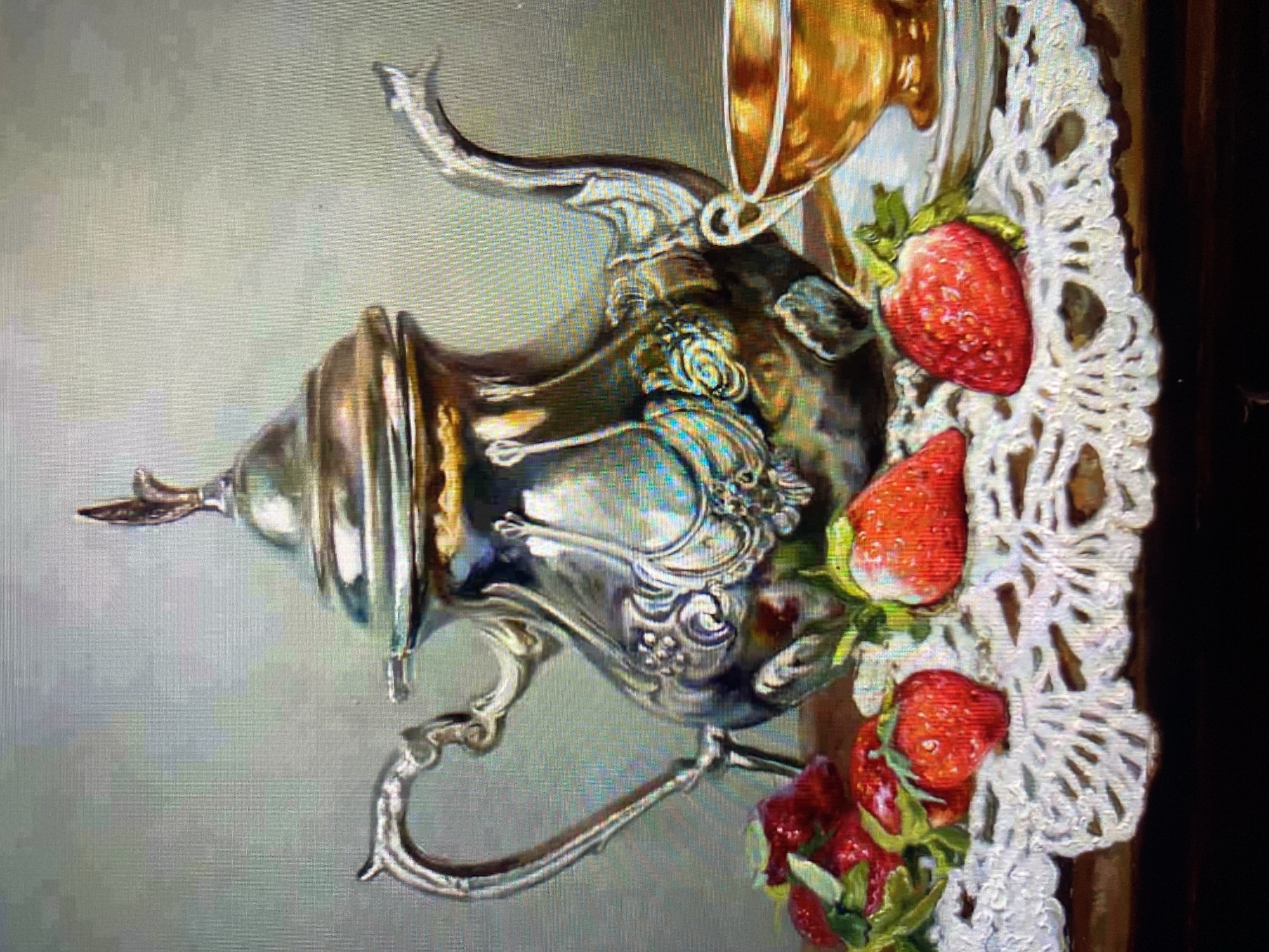 A still life painting depicts a silver teapot, a golden teacup, and several strawberries arranged on a white lace doily. The teapot is ornate, with intricate carvings and a decorative finial. The teacup is placed on a saucer to the right of the teapot. The strawberries are scattered across the doily in front of the teapot. The background is a soft, neutral gray. The painting is rendered in a realistic style with attention to detail and light. The overall impression is one of elegance and abundance.