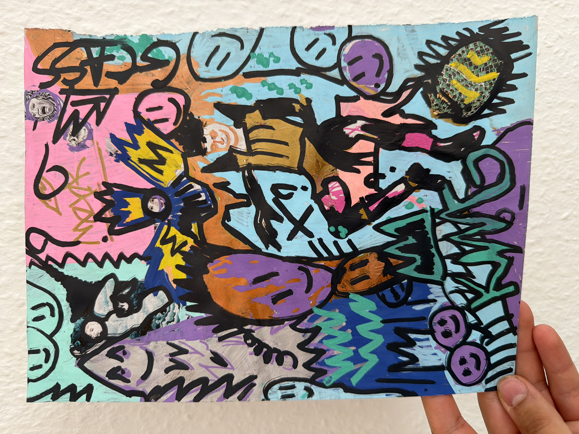 This is a photograph of a mixed-media artwork featuring a vibrant and chaotic composition. The subjects are abstract and cartoonish figures, some resembling faces with simple lines for eyes and mouths. There are also elements that could be interpreted as abstract objects, like a spiky, textured form in the upper right corner with yellow markings, and what appears to be a crown-like structure in yellow and blue on the left.
The artwork is dense with black marker lines over colorful paint, including pink, blue, orange, purple, gold, and green. The style is reminiscent of graffiti or street art, with bold outlines and energetic scribbles. Some areas show a distressed texture, suggesting the use of torn paper or textured paint. There are small photographic cutouts of what appear to be classical busts embedded in the artwork.
The overall mood is energetic and perhaps playful or aggressive due to the strong lines and clashing colors. No specific activity or event is clearly depicted; it seems to be a collection of abstract forms and figures. There are no discernible environmental cues for time of day or weather, and the setting is neutral, as the artwork is presented against a plain white background. There is no visible text in the artwork itself. The photograph is taken in Nienburg/Weser, Germany, with a hand holding the bottom right corner of the artwork.