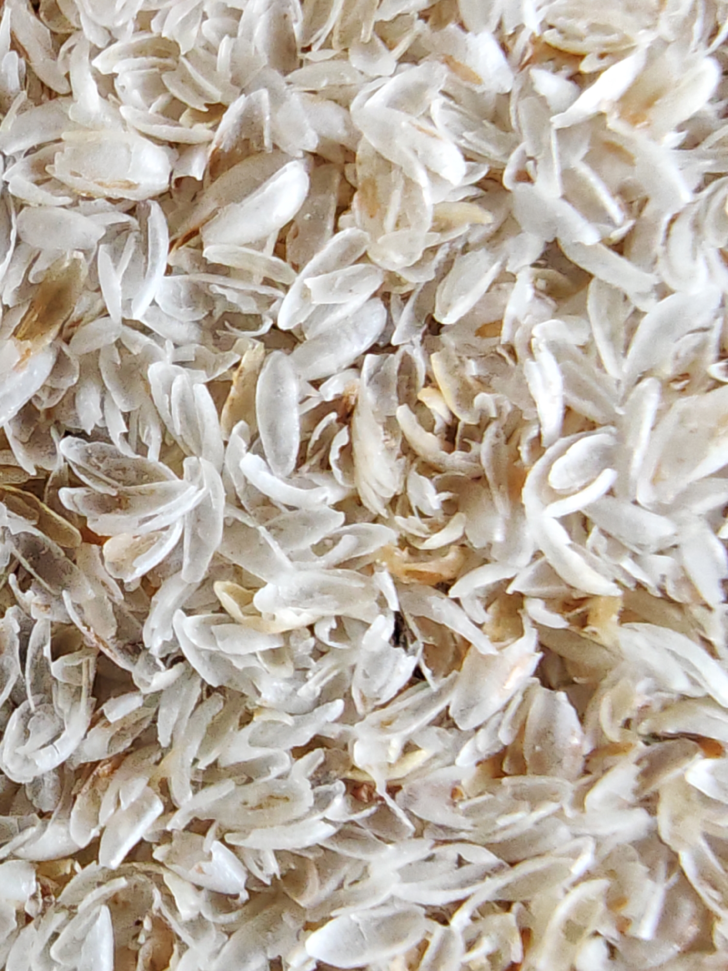 The image is a close-up, overhead shot of a pile of psyllium husk. The husk consists of numerous small, translucent, curved flakes, varying in color from off-white to light tan. Some flakes show a slight brown tint. The texture appears dry and fibrous. There is no indication of a specific location within the city of Kursk, Russia, or any environmental context. The image solely focuses on the psyllium husk.