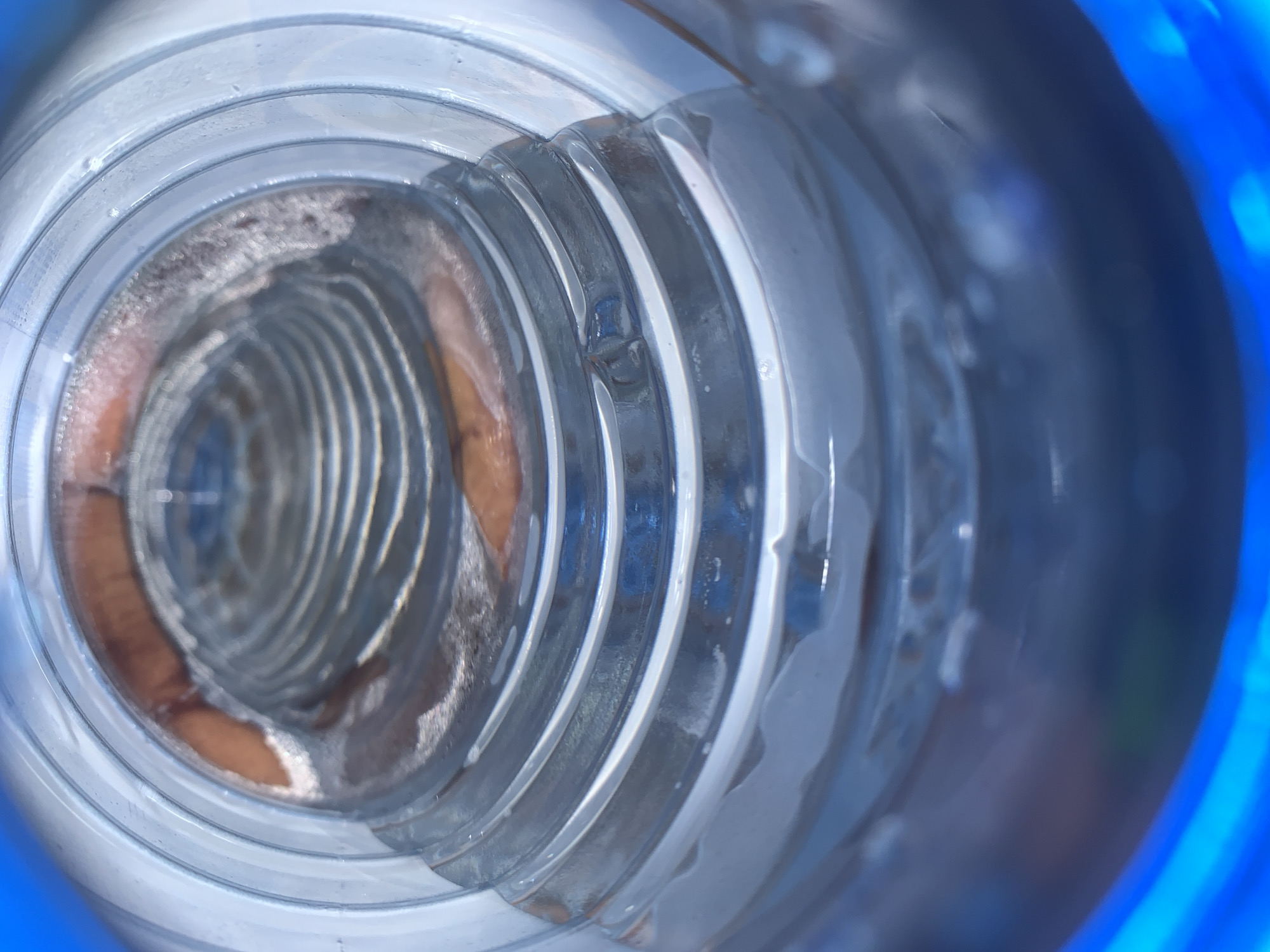 The image shows the interior of a clear plastic bottle, viewed from the opening. The bottle's inner surface has ridges and condensations. Part of a blue object is visible at the outer edge, likely the bottle's exterior. The bottle is located in Jos, Nigeria.