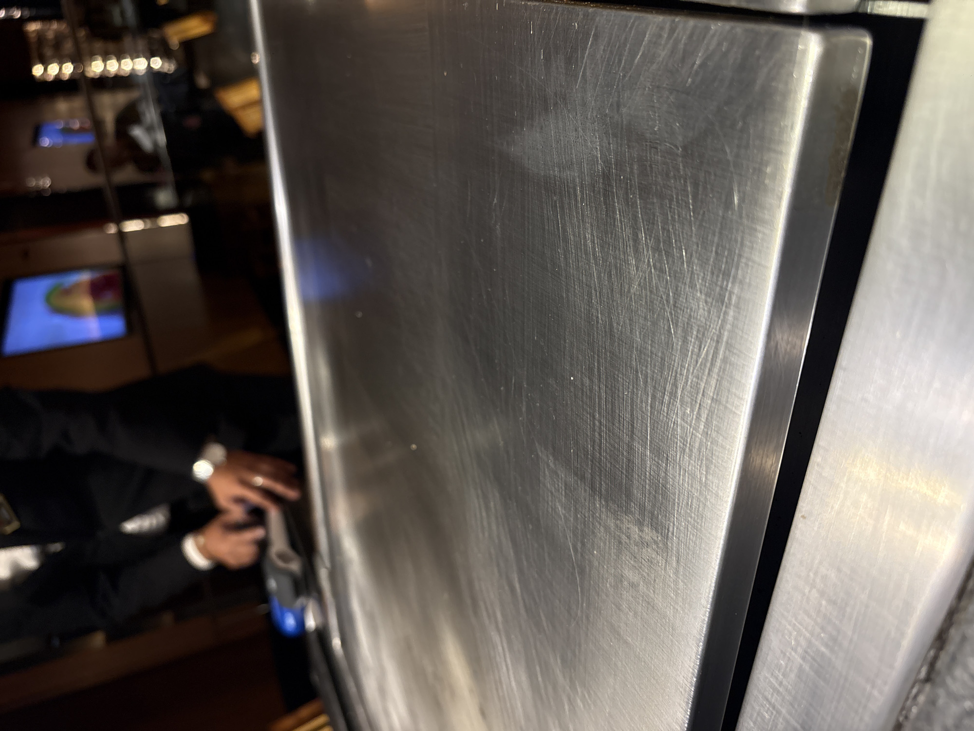 A stainless steel cabinet dominates the foreground of the image. The cabinet's surface is scratched. A person in a dark suit operates a blue and gray device beside the cabinet. In the background, a dimly lit interior shows tables and digital displays. The location is implied to be in Puebla, Mexico.