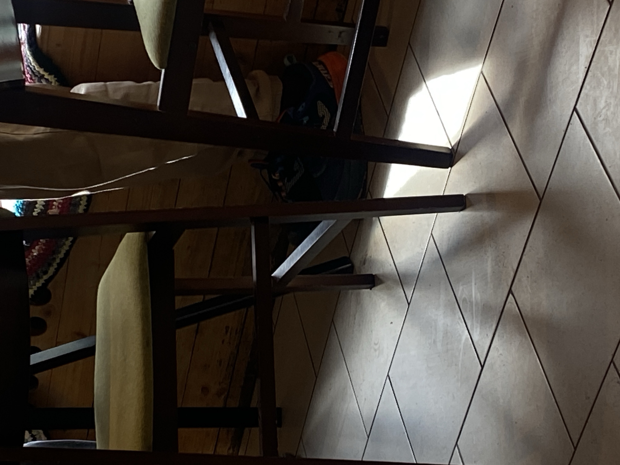 The image shows a close-up, overhead view of two wooden chairs standing on a tiled floor. The tile pattern consists of diamond shapes. A bag with an orange object is visible between the chairs. The chairs have upholstered seats. It is impossible to ascertain the location in the city of Шебунино, Russia, from the image alone.