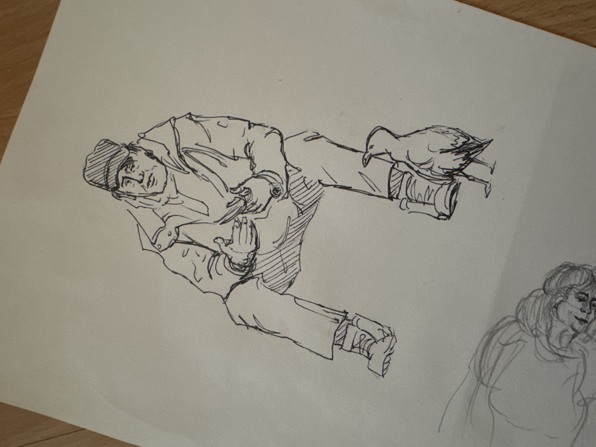 The image is a pen sketch on paper. The main subject is a man in a cap and jacket, possibly a fisherman, lying on his side with his legs bent. A duck or similar bird is perched on his leg near his foot. Another partial sketch of a woman is visible in the lower right corner. The scene's location in Burgas, Bulgaria, cannot be determined from the image.