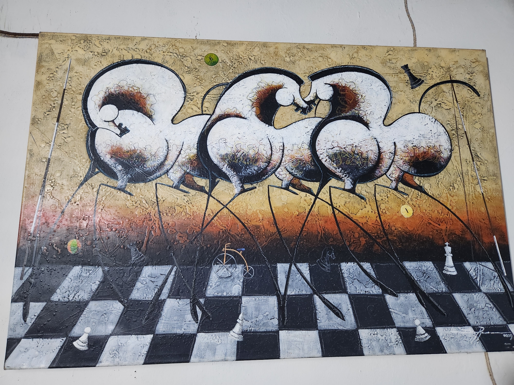 The image is a painting depicting stylized horses on a checkered background resembling a chessboard. The horses are white with dark brown and black details, with elongated, spindly legs. Above the chessboard is a textured, mottled background in shades of tan, brown, and orange. Several chess pieces, including pawns, a rook, and a king, are interspersed on the chessboard. A small bicycle is also present. There is a green circle at the top left of the painting, and a yellow circle on the upper right. The painting appears to be signed at the bottom right with the number 2009. The location is Tinaquillo, Venezuela.