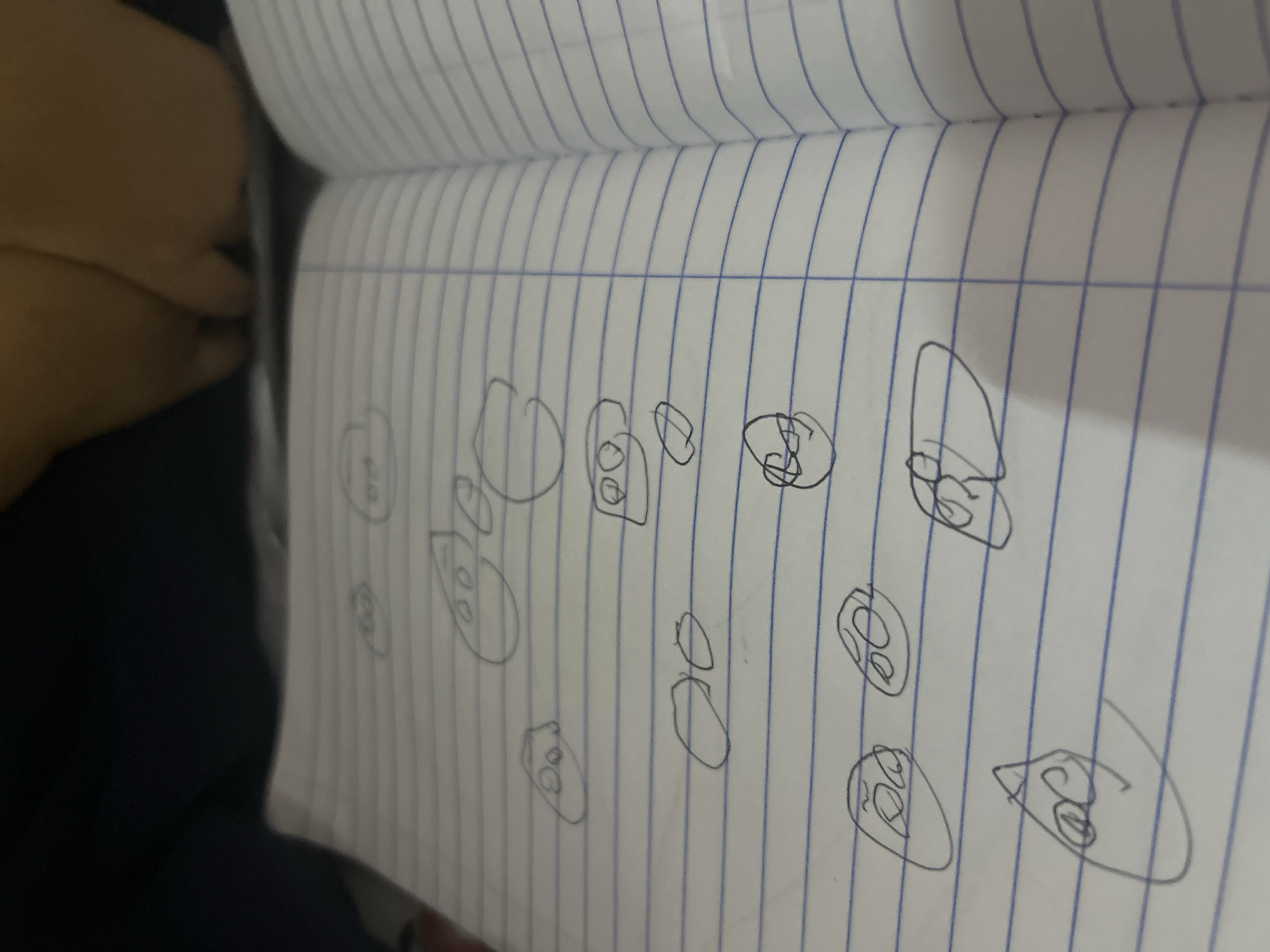 The image shows a notebook with lined paper. Multiple simple doodles of faces are drawn on the paper. No information suggests a location in San Juan de Los Morros, Venezuela or any other specific location. No people or actions are depicted. The environment is limited to the notebook itself.