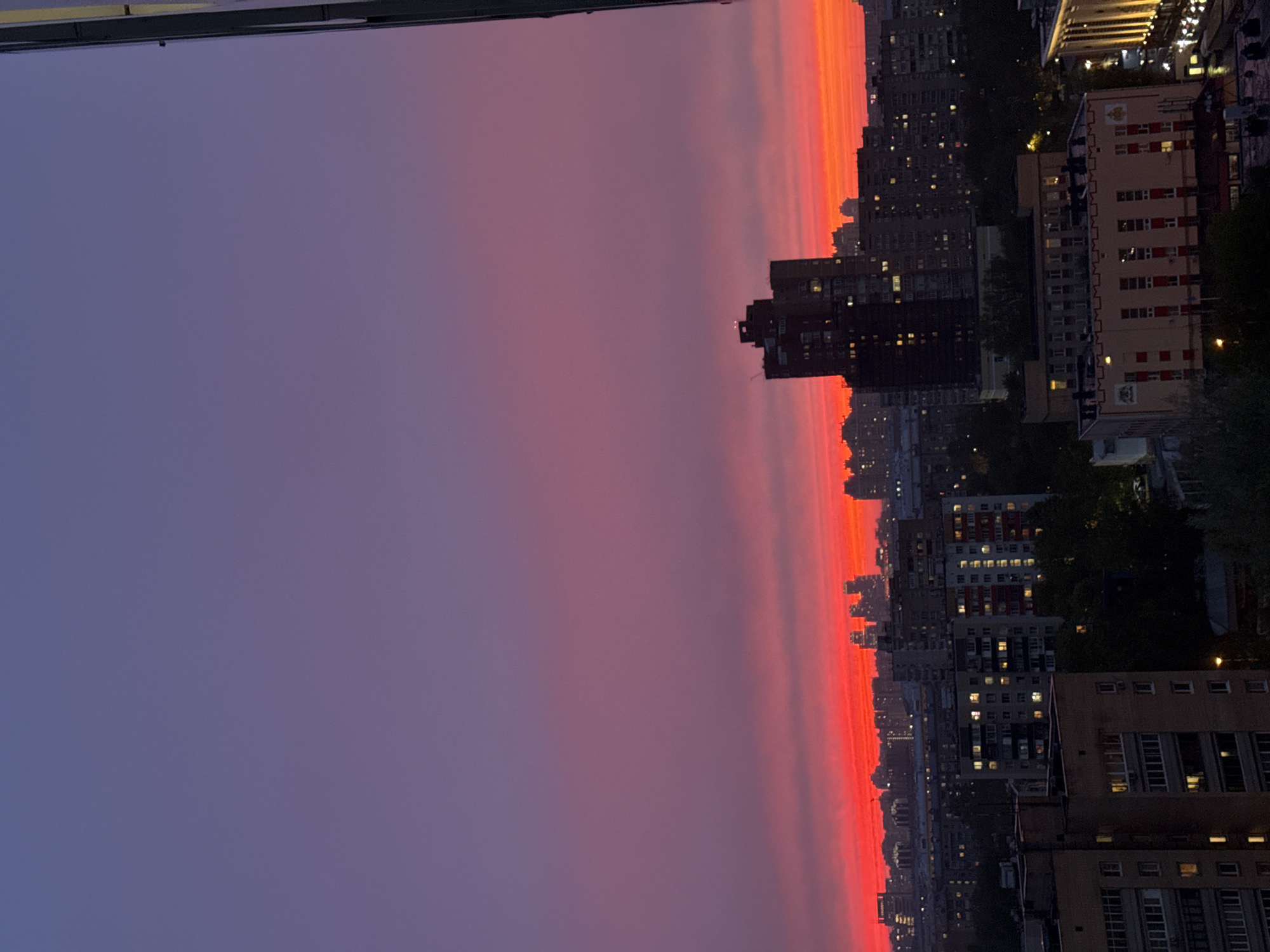 The image shows a sunset over the city of Moscow, Russia. The sky is a gradient of purple and red. There are multiple tall buildings below the horizon. The sky is clear, with no clouds visible.