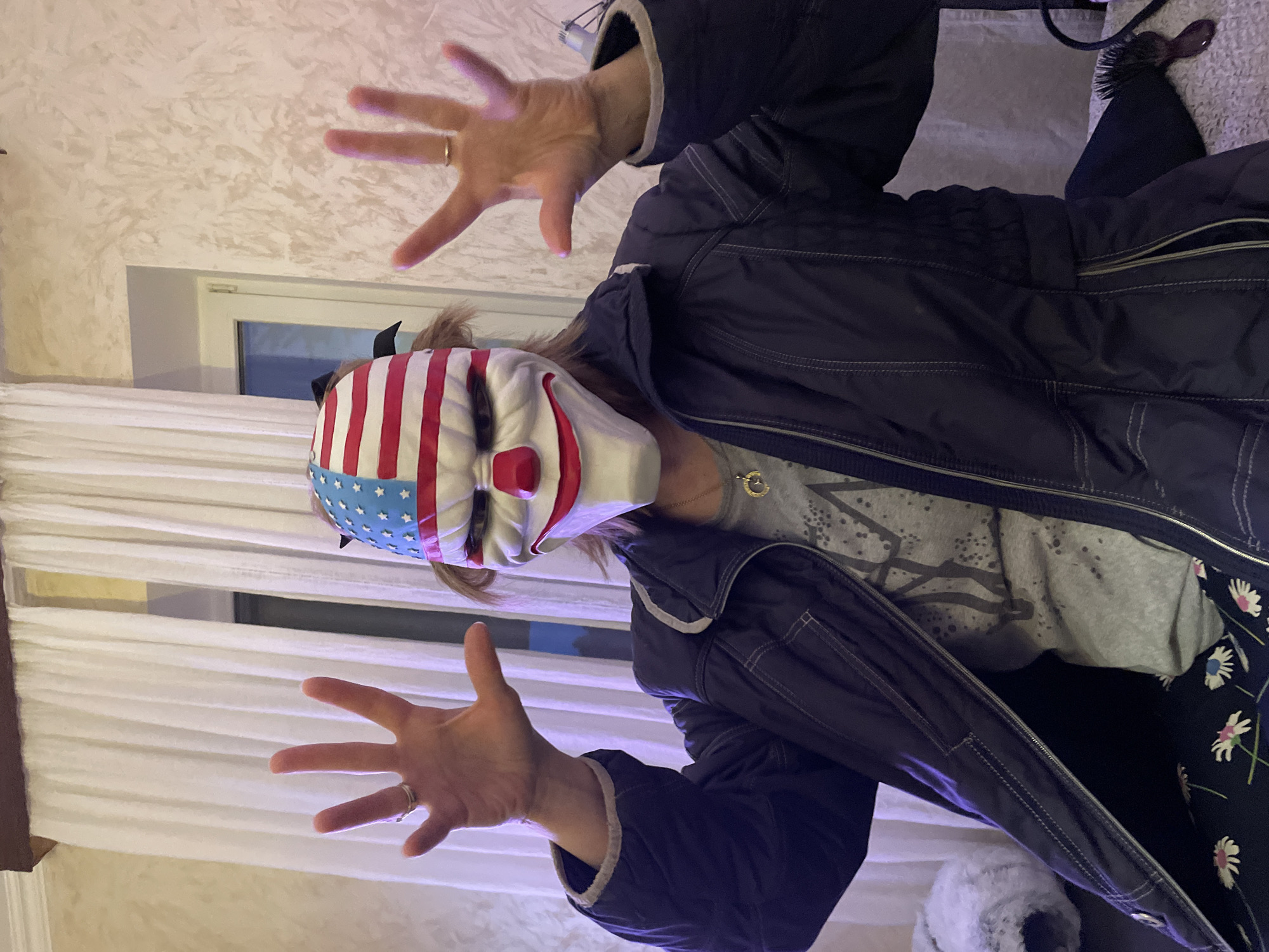 A person wearing an American flag-themed clown mask and a dark jacket is posing with outstretched hands. The scene appears to be indoors, with a window visible in the background. The location is identified as Лесной Пейзаж Кп (шарапово), Russia.