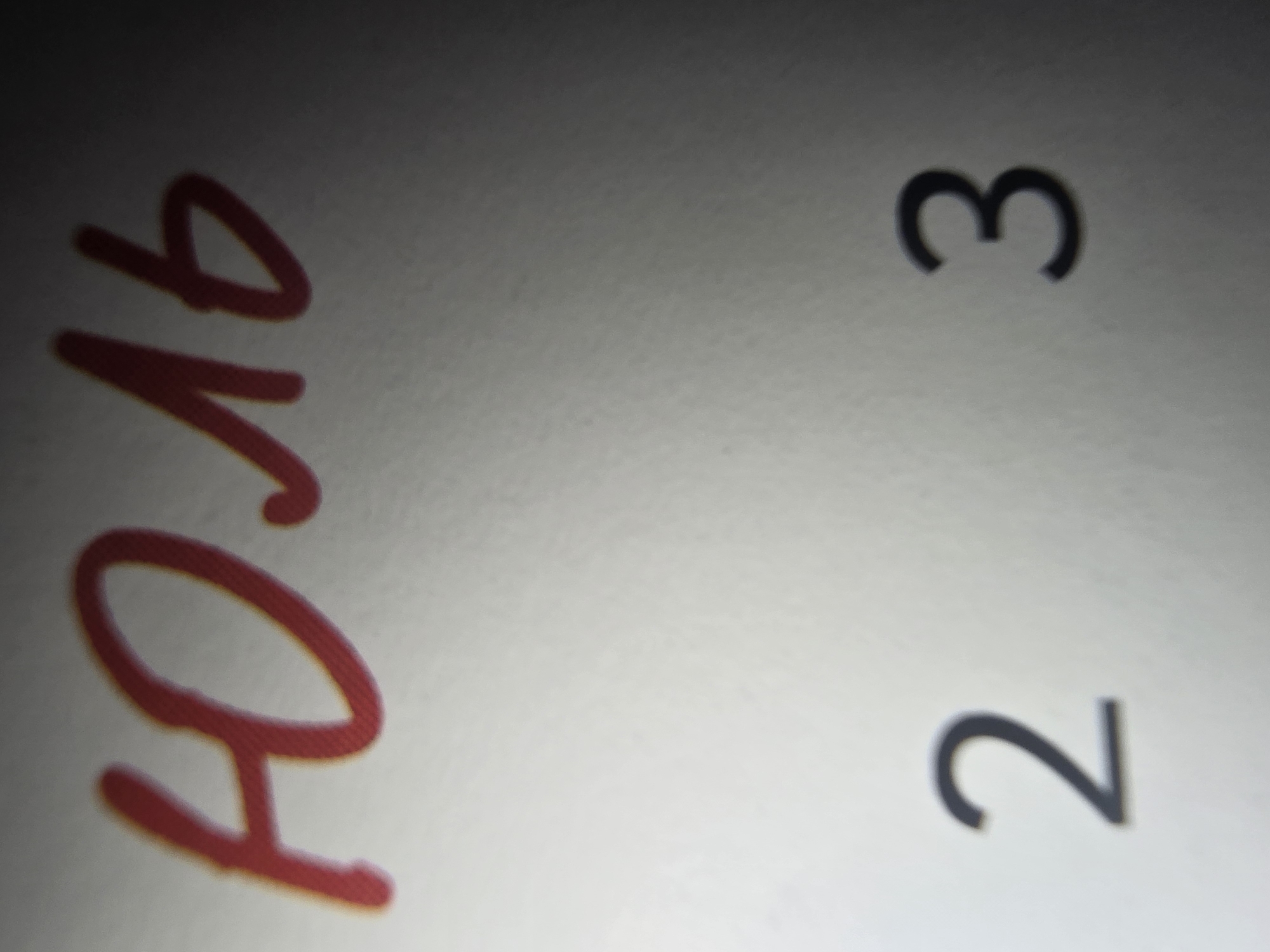 The image displays handwritten text and numbers on a white surface. At the top, in red, is the Russian word "ЮЛЬ". Below this, to the left, is the number "2" in black, and to the right, the number "3" in black. The lighting in the image is uneven, with the top right corner being significantly darker than the rest of the image. There is no discernible urban environment, including any specific locations within Ulan-Ude, Russia.