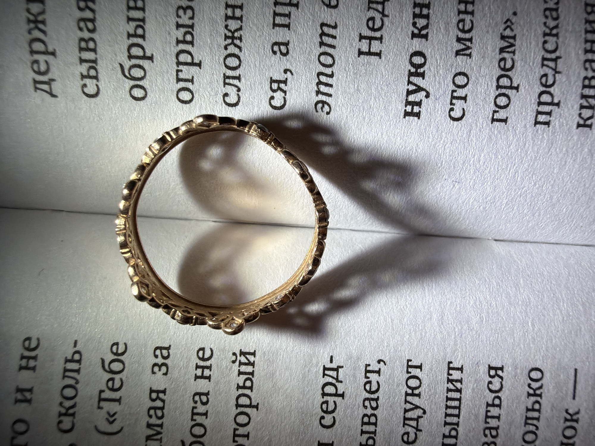 A close-up shot shows a gold ring resting on a page of text, casting a shadow on the page. The text is written in a language that appears to be Russian. The scene takes place in Unknown, Unknown.