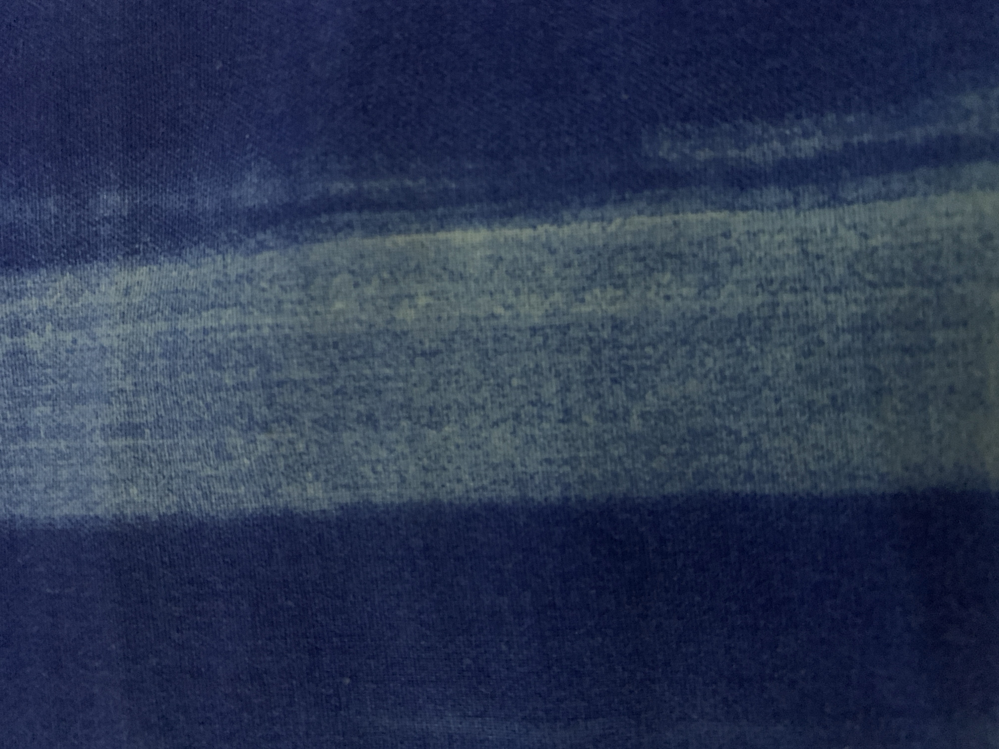 The image shows a close-up view of fabric with a horizontal stripe pattern. The fabric appears to be a knit material. The colors present are various shades of blue, with a darker blue dominating the top and bottom portions, and a lighter, faded blue in a horizontal band in the center. The texture of the fabric is visible.