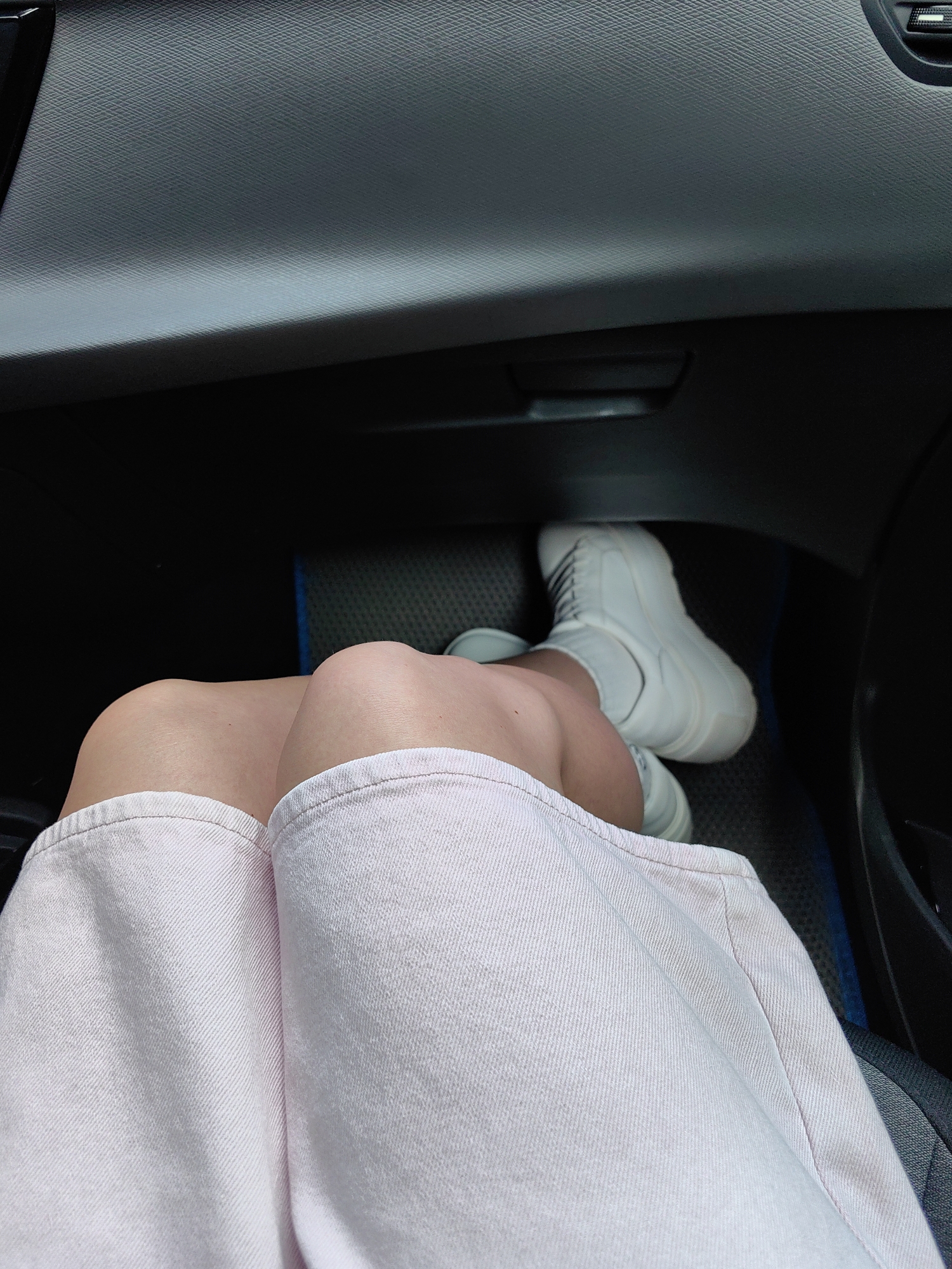 The image shows a close-up view of a person's legs inside a vehicle. The person is wearing a light pink skirt and white high-top sneakers. The background consists of the car's interior, including the dashboard and a floor mat. The lighting suggests it is daytime, and the scene appears to be captured from a seated position within the vehicle. The location of Хаценчыцкі сельскі Савет, Belarus is not depicted in this image.