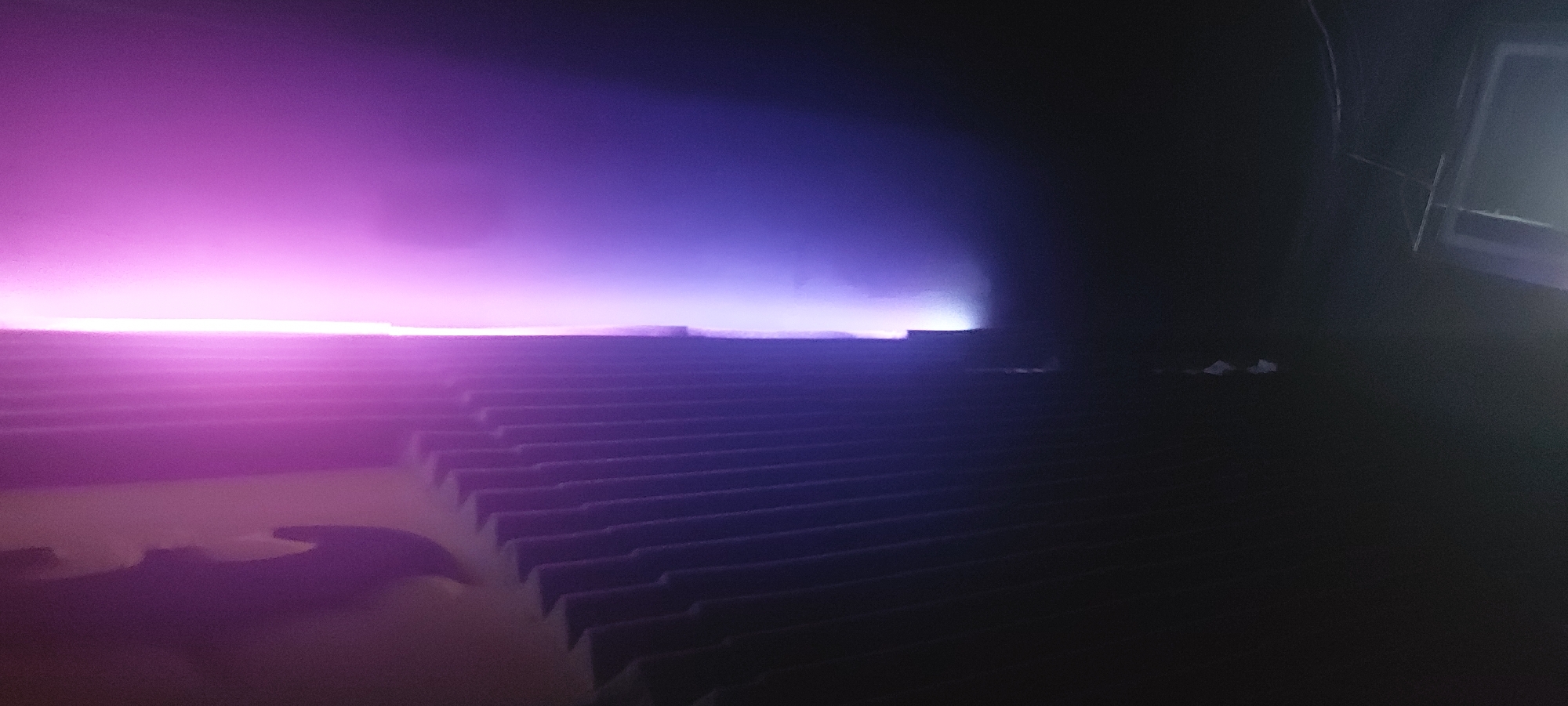 The image depicts a set of tiered metal steps illuminated by a strong violet and purple light source originating from the left. The steps fade into near total darkness on the right side of the frame. In the far background, partially obscured by the darkness, is a window frame. There are no people visible. There is no information in the image that would indicate that it was taken in Tashkent, Uzbekistan.