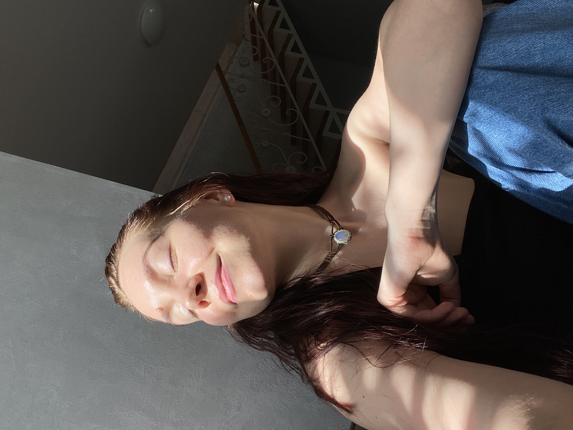 A woman with long, dark auburn hair and fair skin is resting. She is lying indoors. She is wearing blue jeans. The location is unidentified and not suggested in the image.