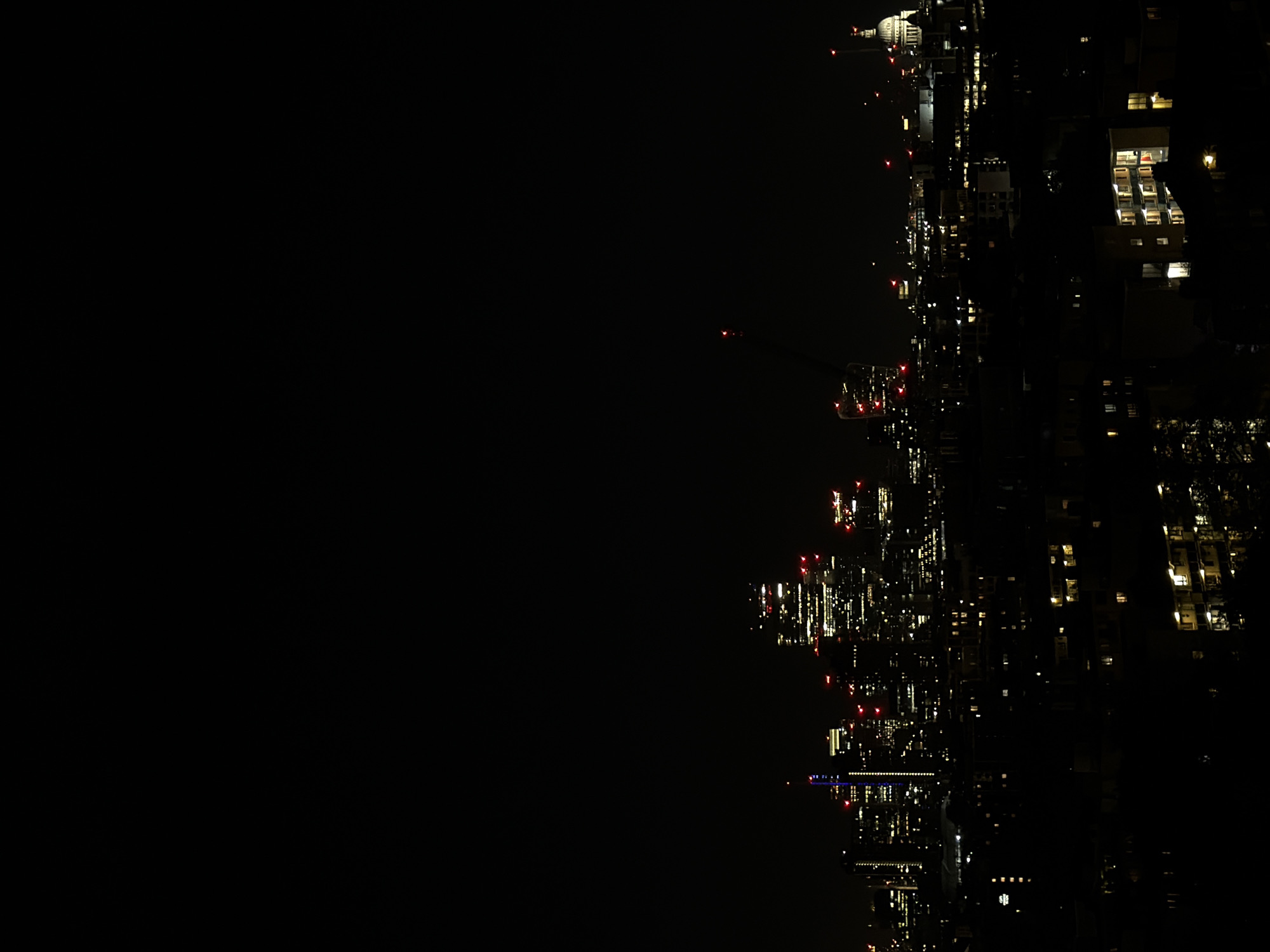 The image shows a nighttime view of London, United Kingdom. The right side of the image depicts an aerial view of the city illuminated by streetlights and building lights. St. Paul's Cathedral can be seen in the upper right. The left side of the image is mostly dark, contrasting sharply with the lit-up cityscape.