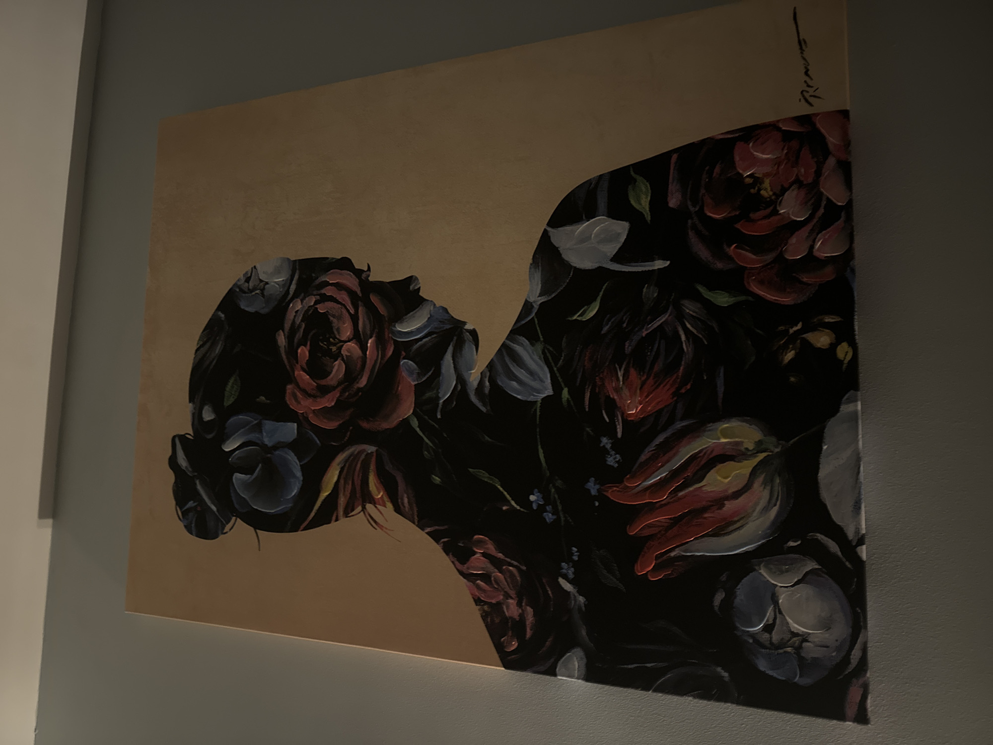 A close-up shot shows a painting hung on a gray wall. The painting features a profile of a person's head and upper torso, which is filled with a dark floral pattern. The background of the painting is a solid tan color. The painting has a signature in the upper right corner. The setting appears to be an interior space with natural light. No specific location in Sofia, Bulgaria, can be determined from the image.