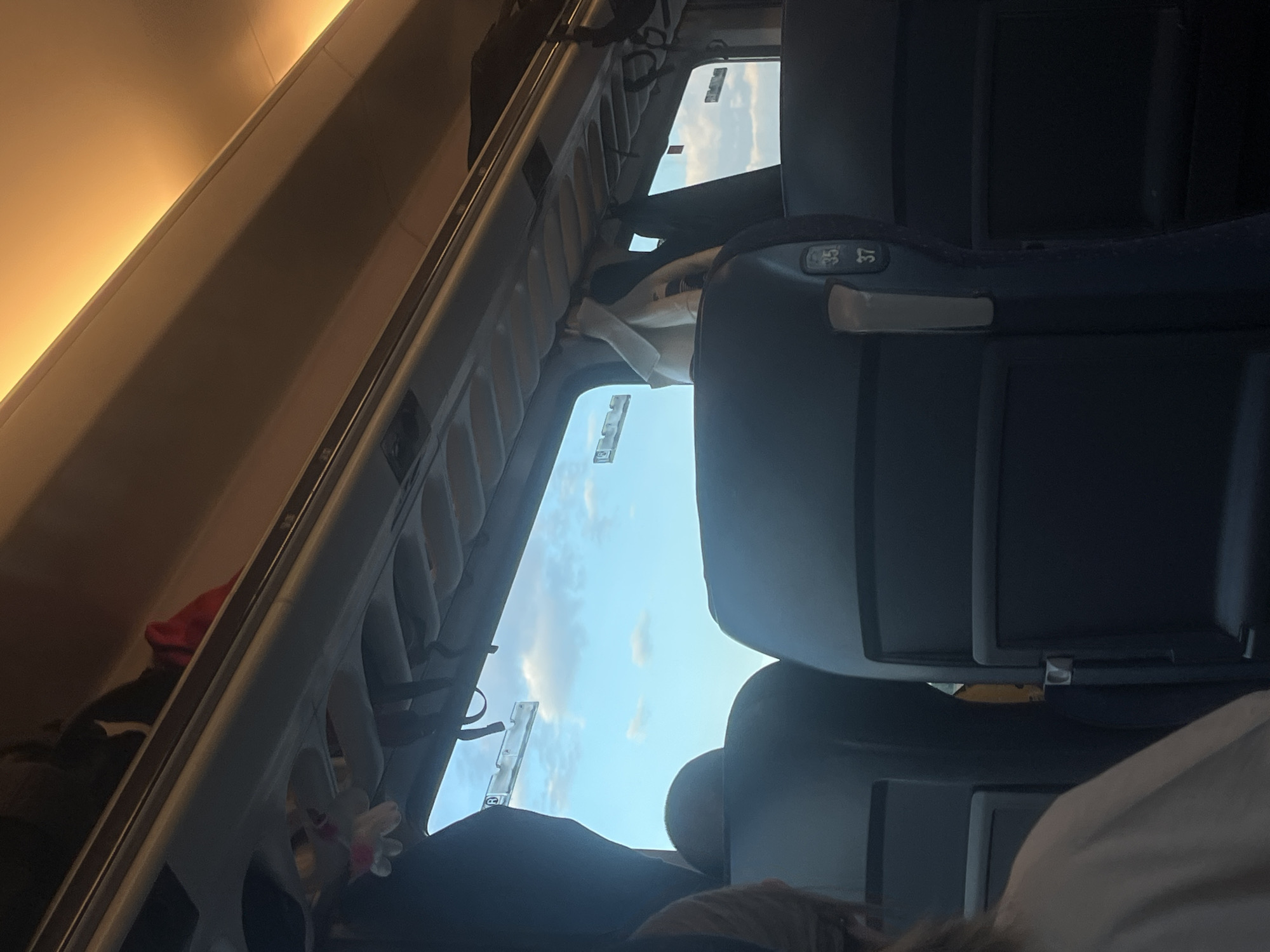 Interior view of a train car. Seats are visible, with seat numbers "35" and "37" displayed. Luggage racks are overhead, some containing items. The train windows offer a view of the sky with clouds. The image is rotated counterclockwise.