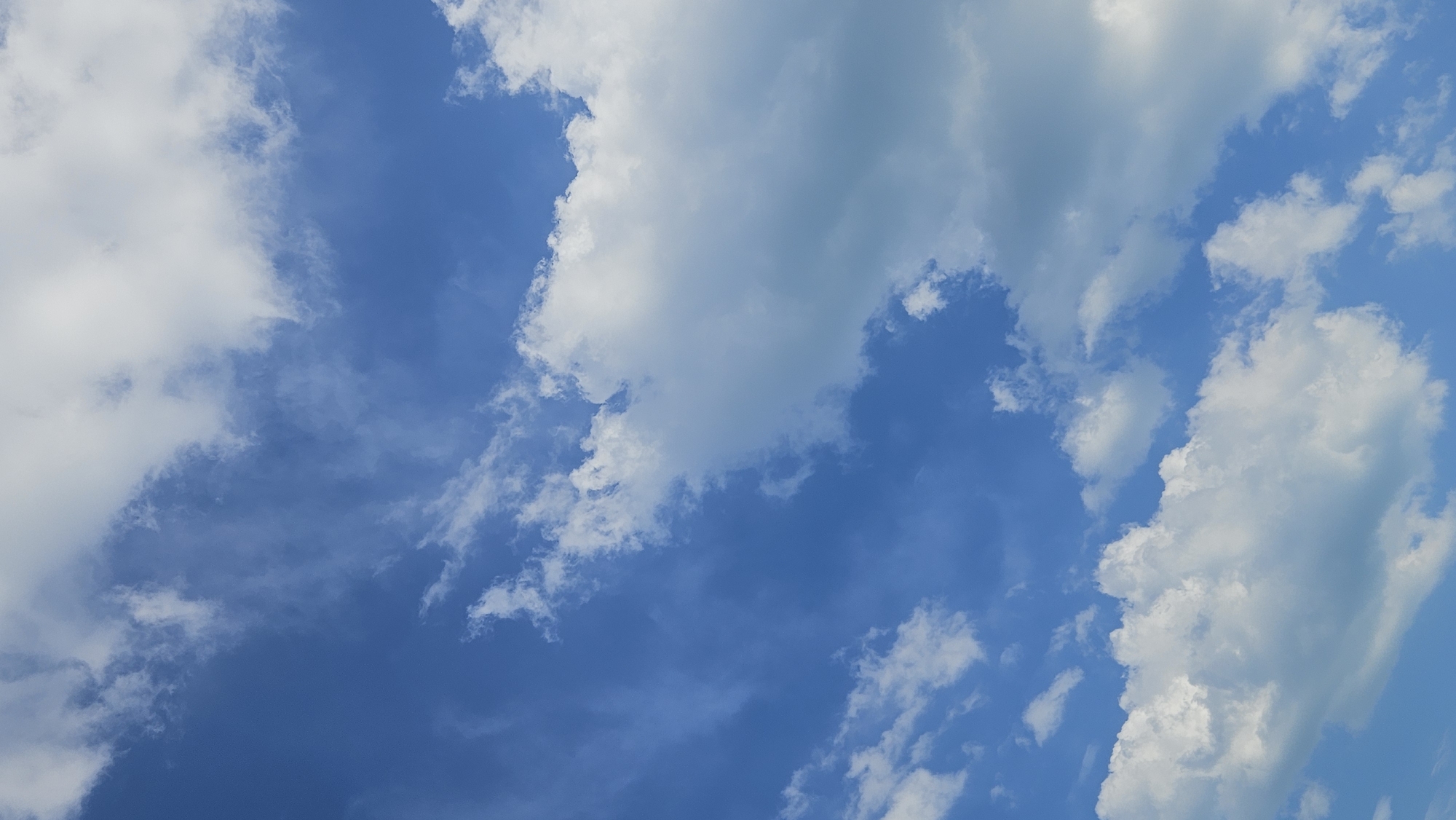 The image depicts a clear blue sky with scattered white clouds. The clouds are of varying sizes and densities, with some appearing wispy and thin, while others are larger and more voluminous. The sunlight illuminates the clouds from above, casting shadows and creating depth. The overall impression is one of a bright and pleasant day. There are no people, structures, or specific landmarks visible in the image, making it impossible to determine its location within Dyurso, Russia or any other geographical area.