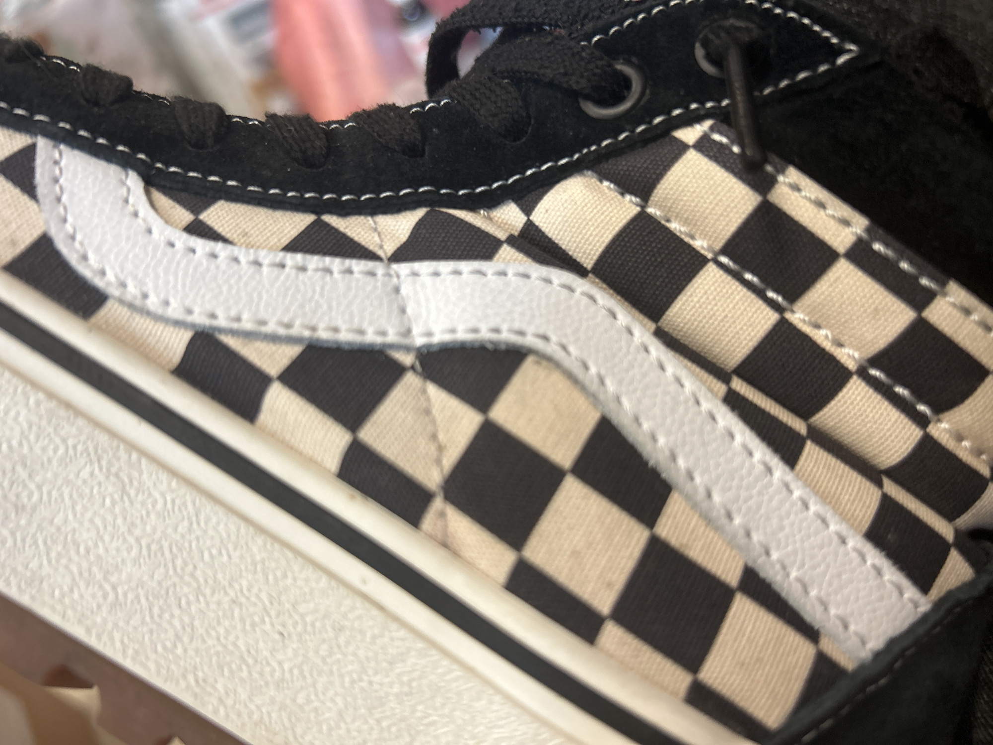 A close-up view of a Vans sneaker, specifically a model with a black and white checkerboard pattern on the side panel. The iconic white leather side stripe is prominently displayed. The shoe has black laces, a black suede toe cap, and a white midsole with a black stripe. The image does not provide location data to determine if this is in Sofia, Bulgaria.