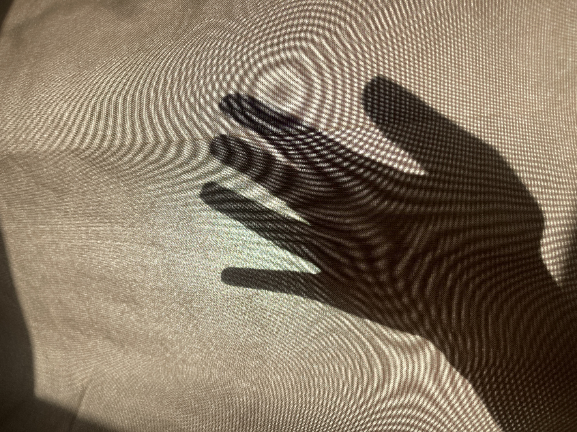 A shadow of a human hand is cast upon a textured, semi-transparent fabric. The lighting is soft, allowing some light to pass through the fabric. The fabric appears to be slightly wrinkled or draped. No information is available in the image to indicate the location in Мосметаллоконструкция Онт, Russia.