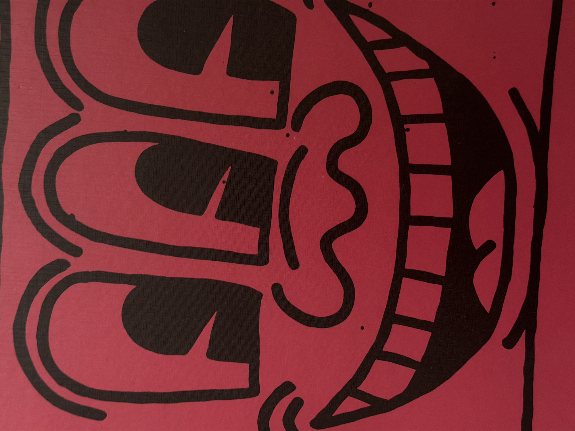 The image shows a detail of a cartoon-style artwork, possibly a mural or painting, featuring a stylized face. The face is composed of bold black outlines on a red background. Key elements include large rectangular eyes, an ear depicted as a simple wavy line, and a wide, toothy grin. The image is a close-up, focusing on a portion of the artwork. There is no indication of people, objects, actions, interactions, or the environment to make a relationship between this and the city of Khimki, Russia.