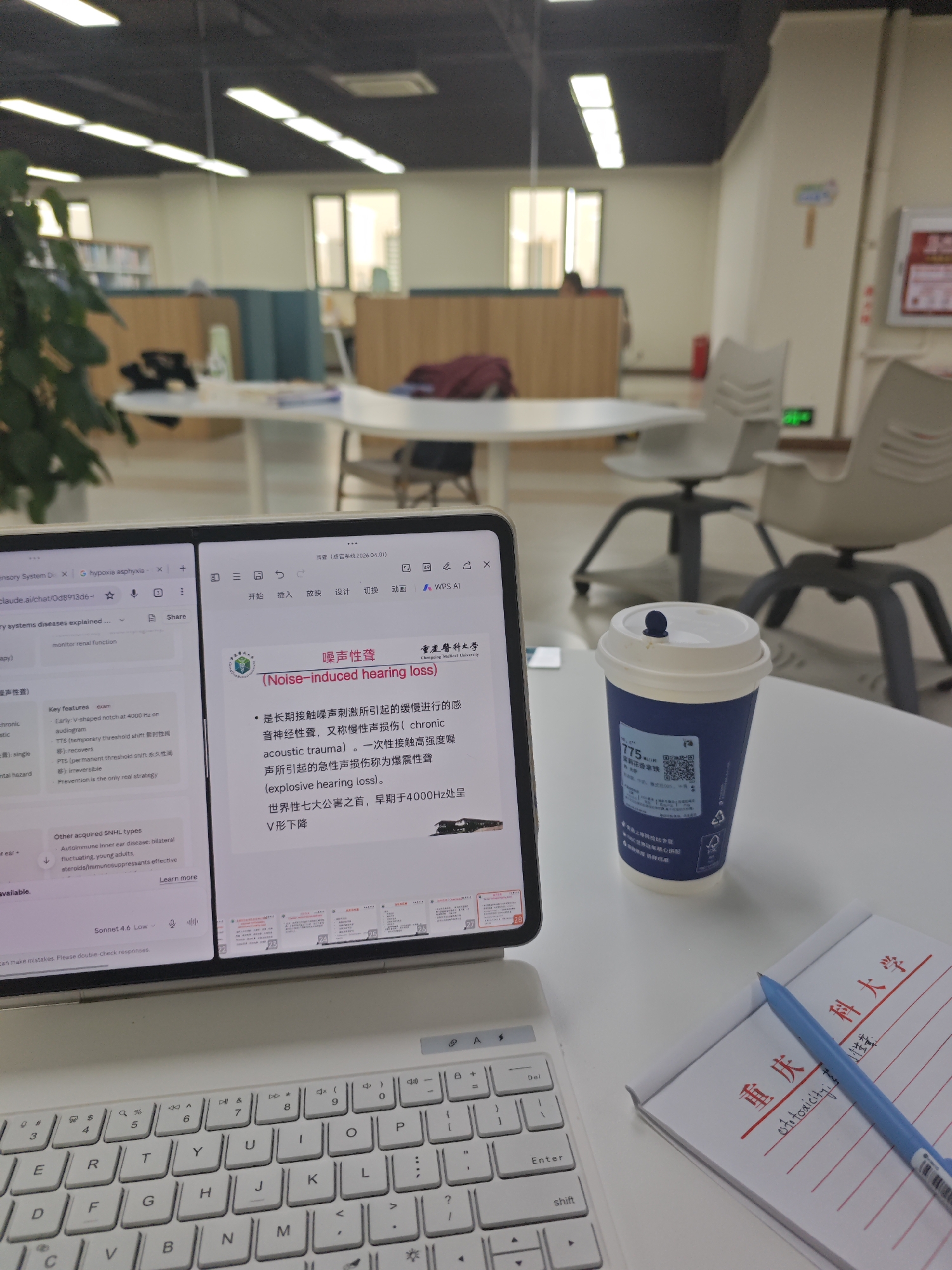 The image depicts a close-up of a laptop screen displaying two open tabs, a coffee cup, a notepad with writing, and a keyboard. The left tab on the laptop shows a webpage with text in English and a portion of a presentation slide. The right tab shows a presentation slide with Chinese text and an image. The coffee cup is blue and white with some text and a QR code. The notepad contains handwritten Chinese characters in red ink and some English text in blue ink. A blue pen rests on the notepad. The keyboard is white and appears to be part of a laptop or tablet setup. The background suggests an indoor environment, possibly a library or study area, with desks and chairs visible, and fluorescent lighting. The overall scene suggests a moment of study or work.