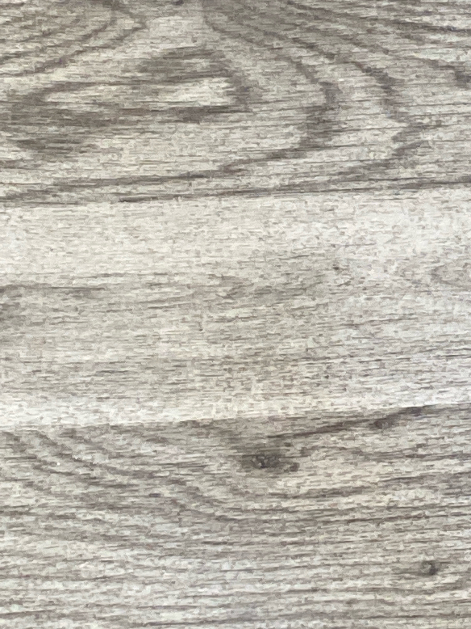 The image is a close-up, full-frame, vertical shot of a weathered, grey-toned wood grain surface. The grain exhibits a pattern of parallel lines with subtle variations in shading and texture, suggesting age and exposure. There are no discernible objects, people, or actions within the frame. The lighting appears to be diffuse, casting no strong shadows and highlighting the textural nuances of the wood. The scene is abstract, focusing solely on the natural pattern of the material. There is no information within the image to associate it with Broxbourne, United Kingdom or any specific urban location.